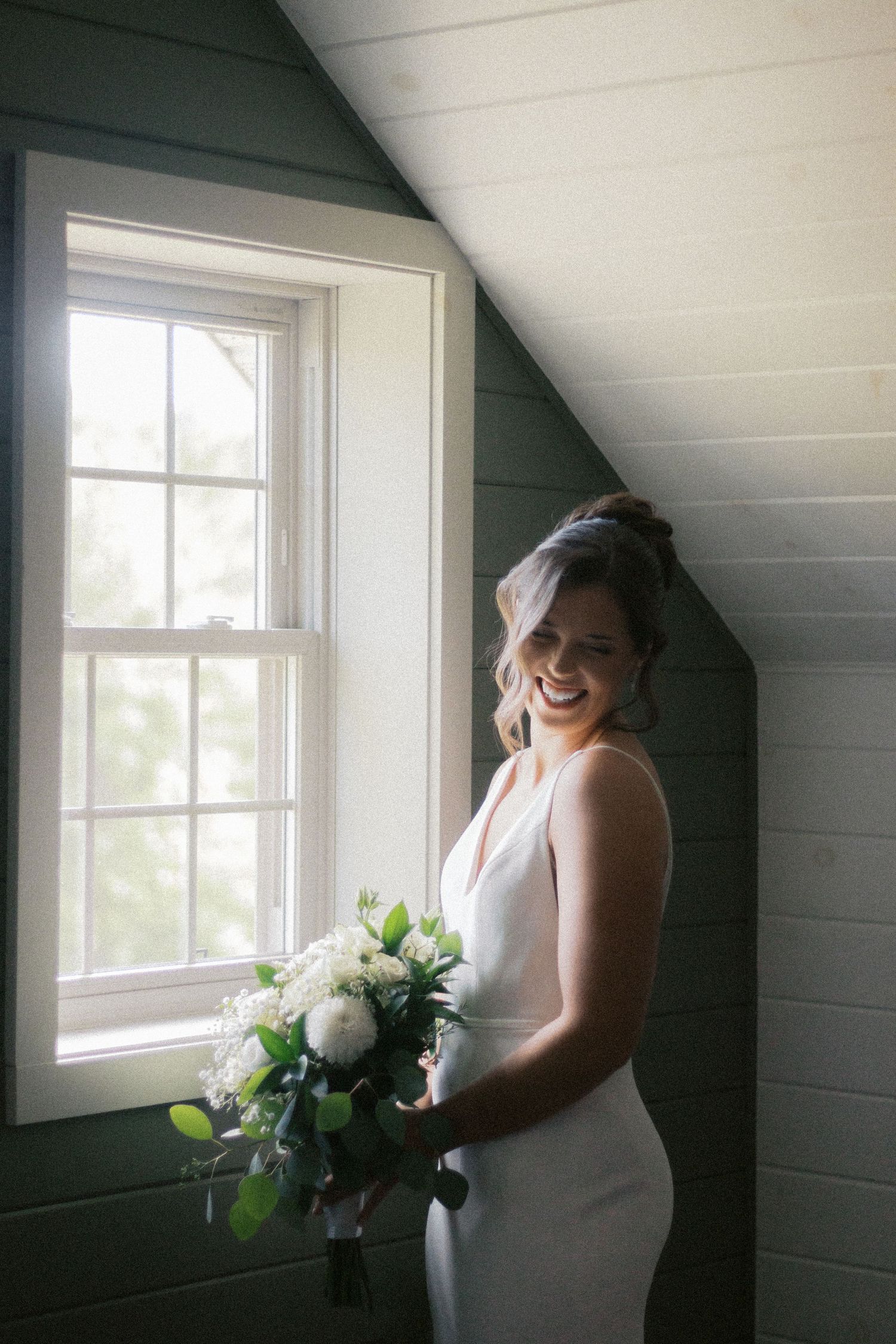 Intimate bridal moment captured by window light in rustic room setting.
