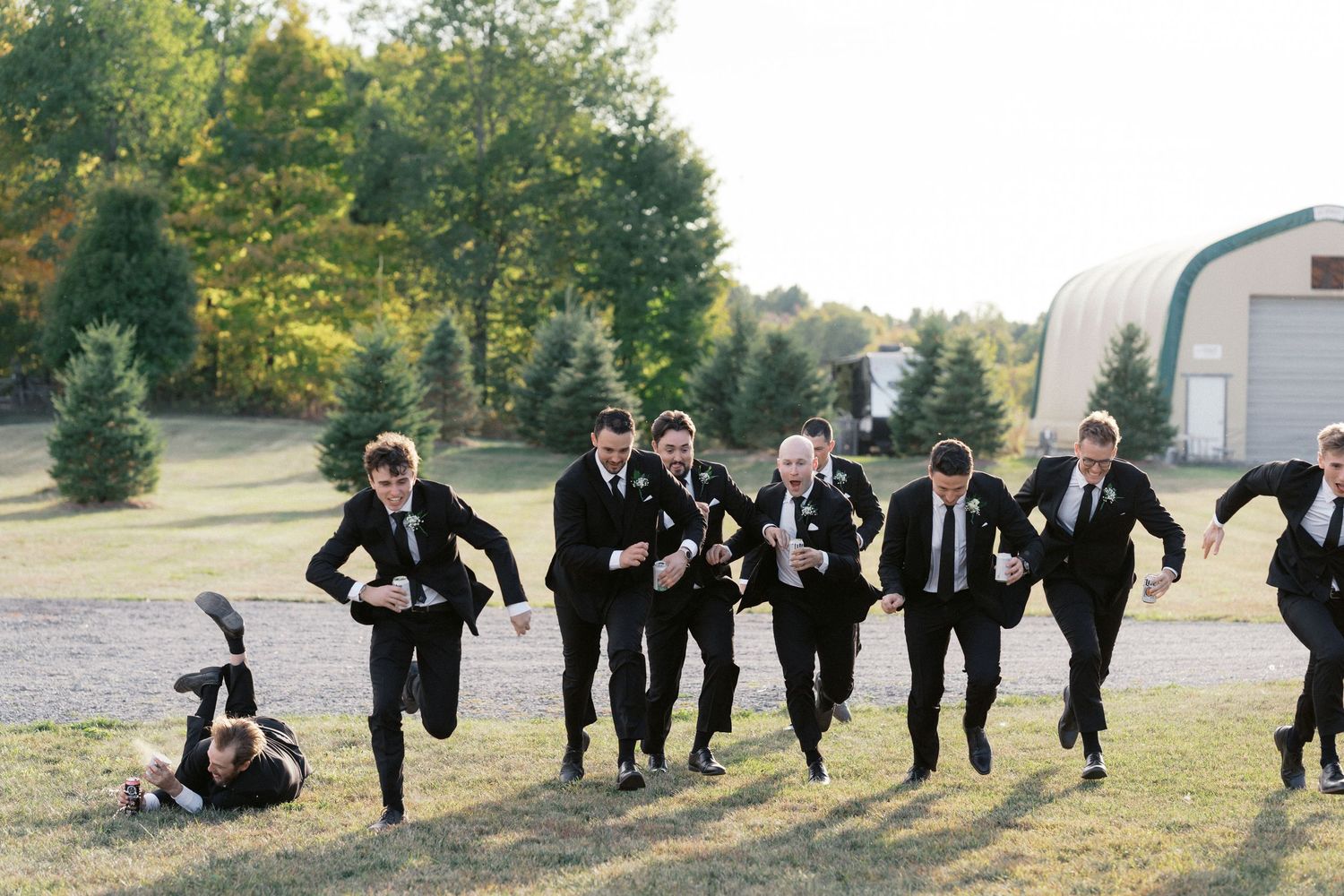 Groomsmen in black suits running playfully across a grassy field.