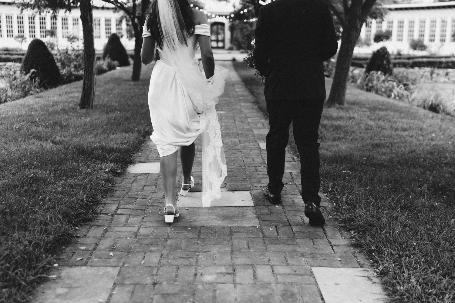 Wedding party members walk together on a stone pathway during formal photo session.