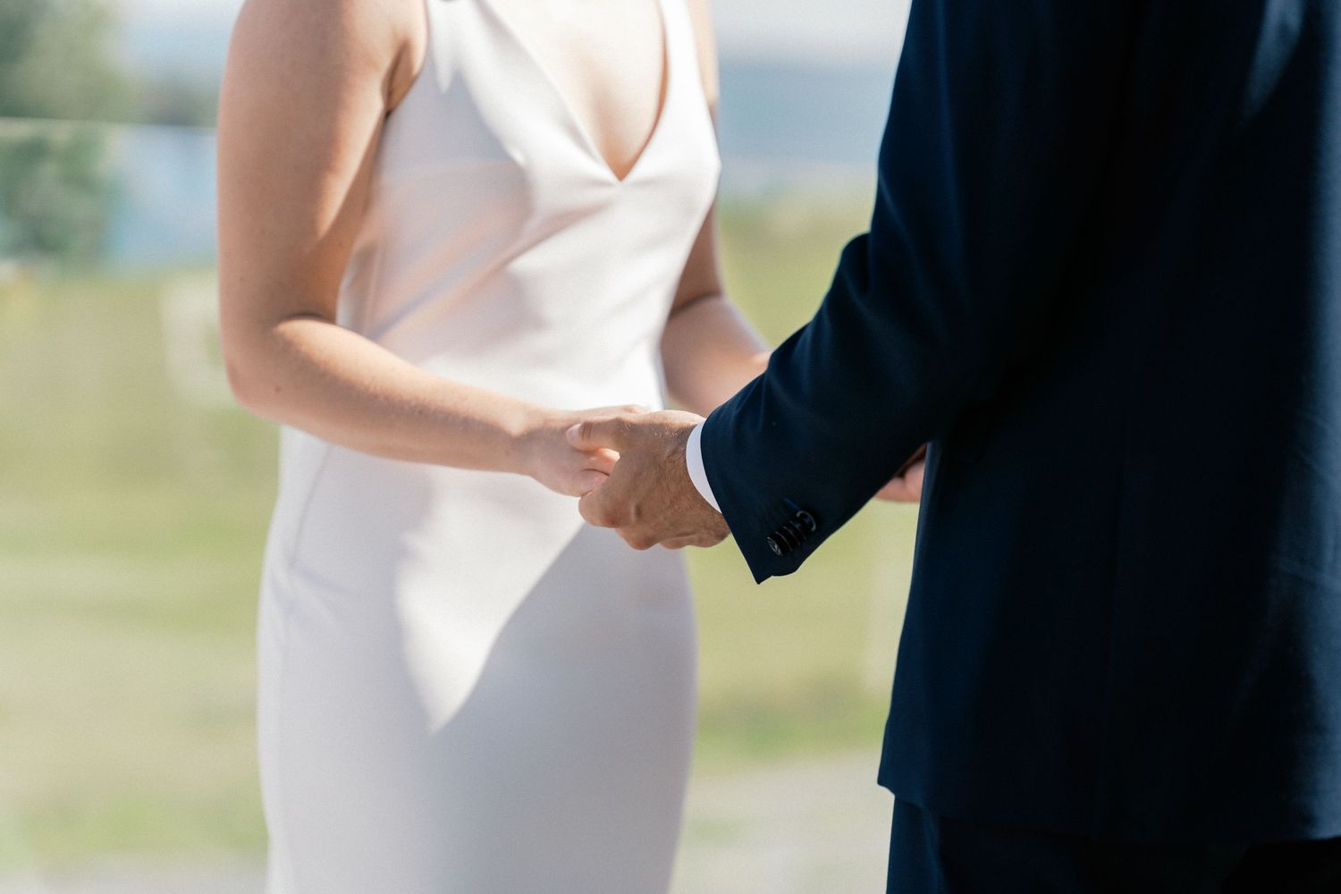 Bride and groom holding hands during wedding ceremony, bride wearing elegant white sleeveless gown.