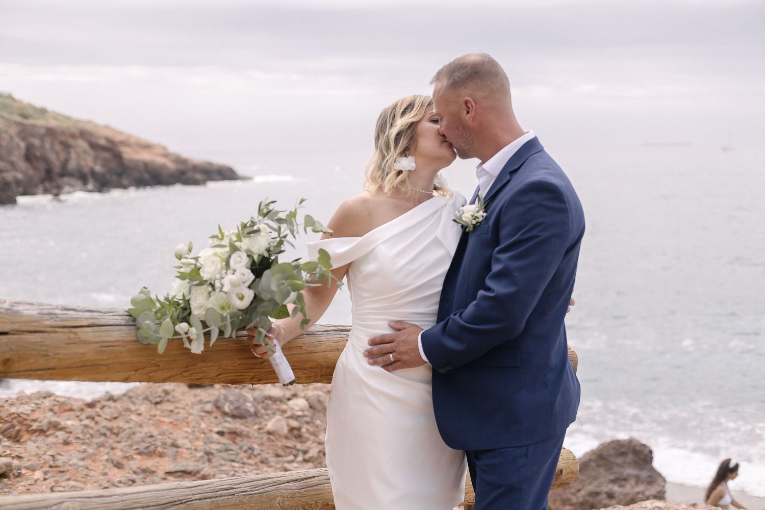 A wedding couple shares an intimate moment together on a cliff overlooking the ocean.