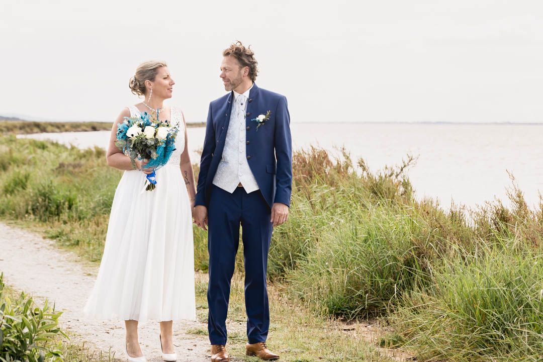 Wedding couple poses together on coastal grassy dunes with ocean backdrop.