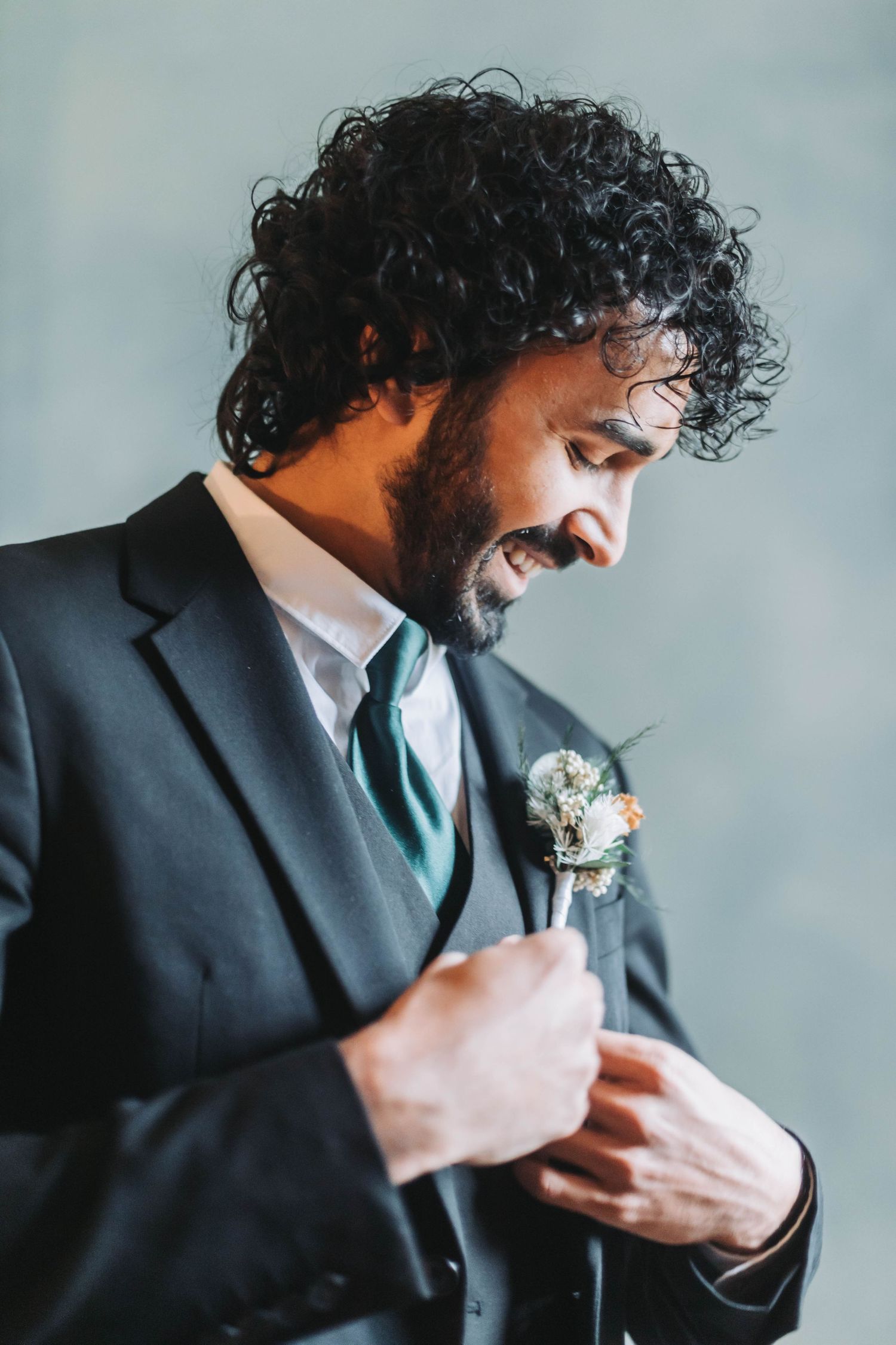 Person in dark formal suit adjusting their boutonniere against light background.