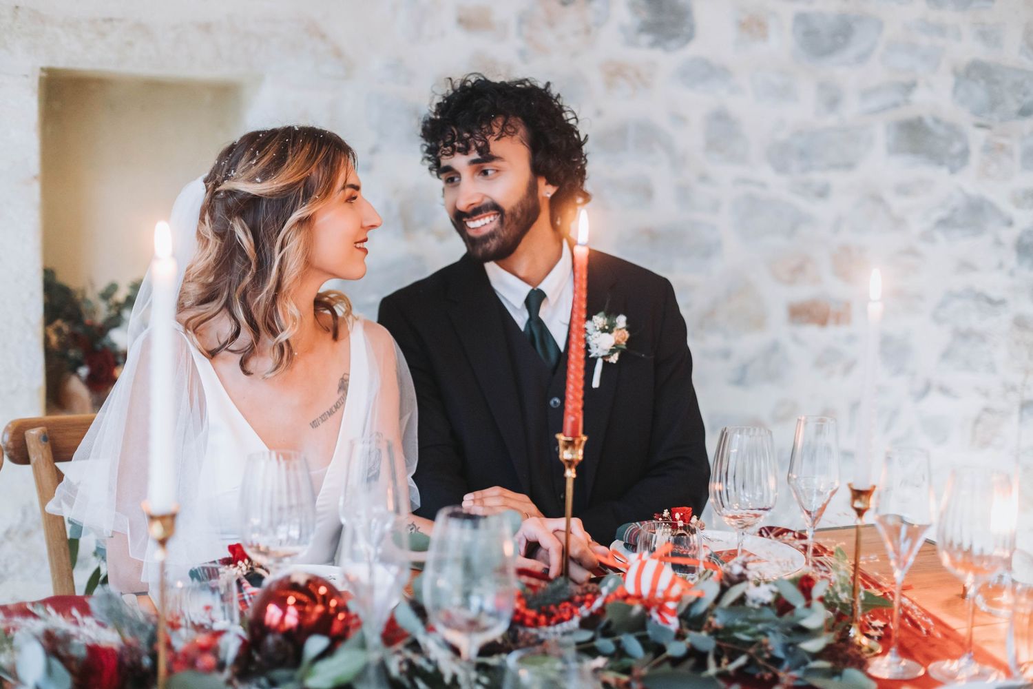 Romantic wedding table setting with couple dining among red candles and floral decorations.