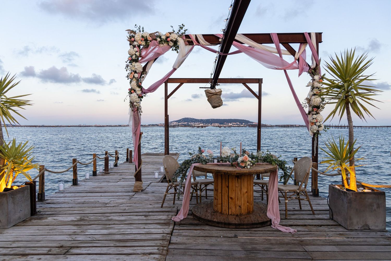 Scenic oceanfront wooden deck decorated for a wedding ceremony with palm trees and water views.