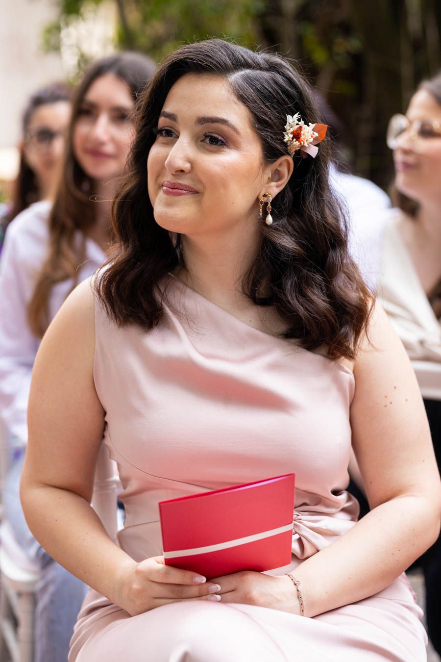 Woman in pink dress holding a red book during special occasion.