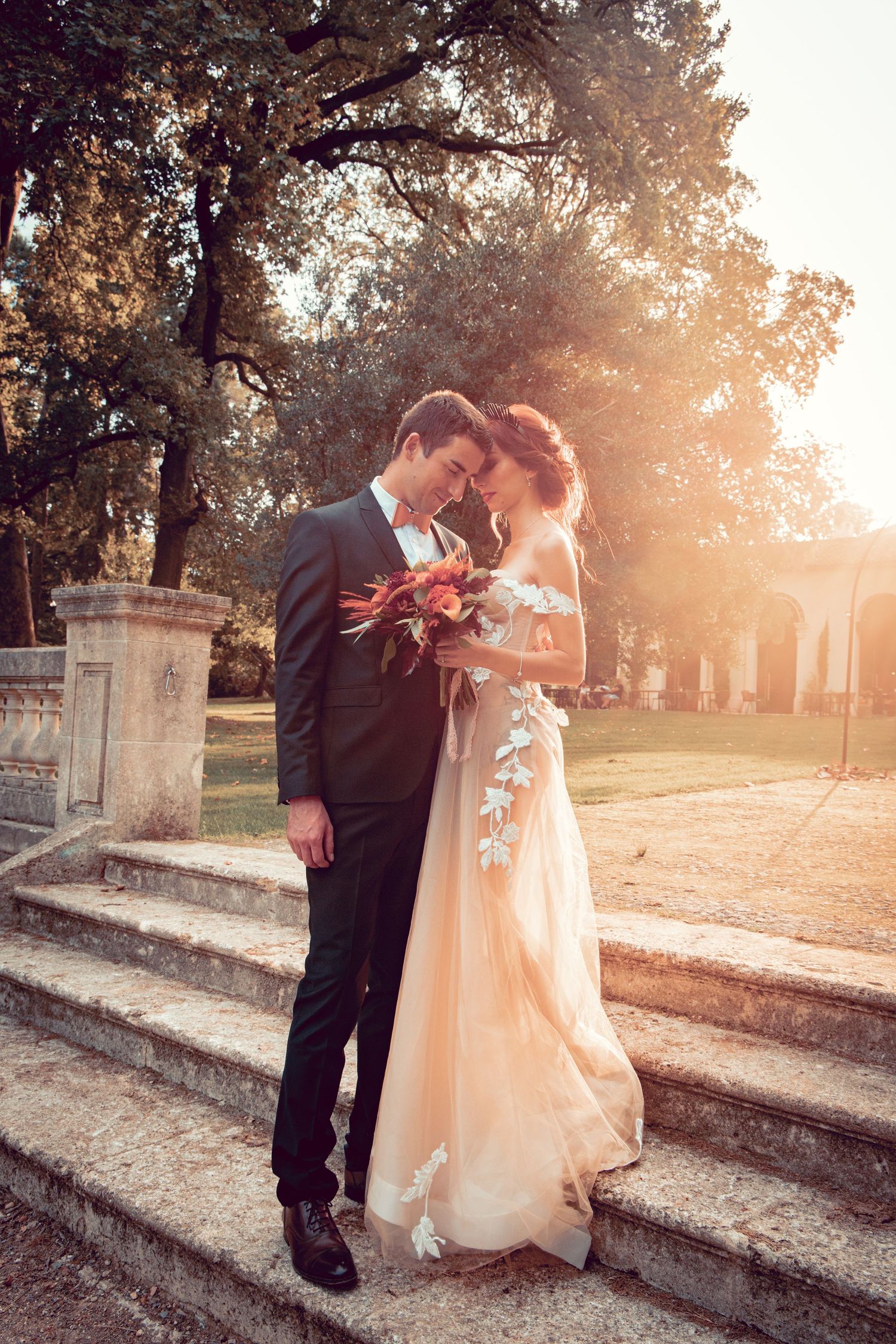 A romantic couple embraces on stone steps at sunset in a garden setting, creating a dreamy wedding moment.