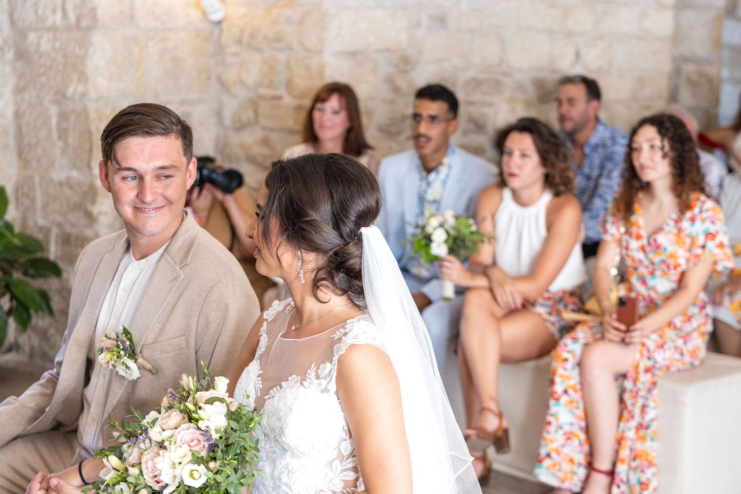 Joyful wedding celebration with guests in floral dresses inside stone-walled room.