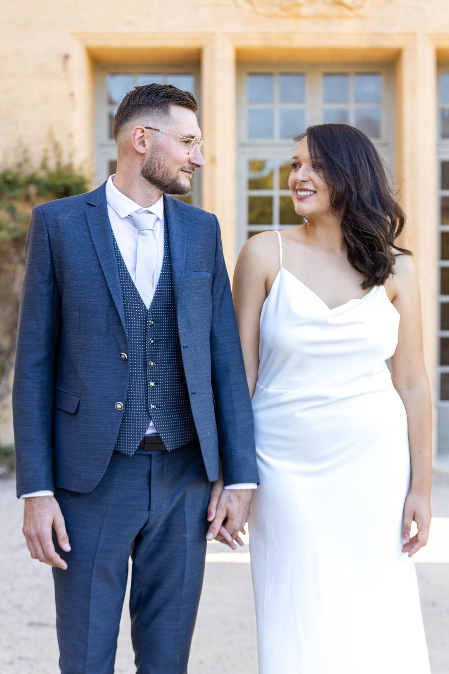 A couple in wedding attire sharing joyful moments against a stone building exterior.