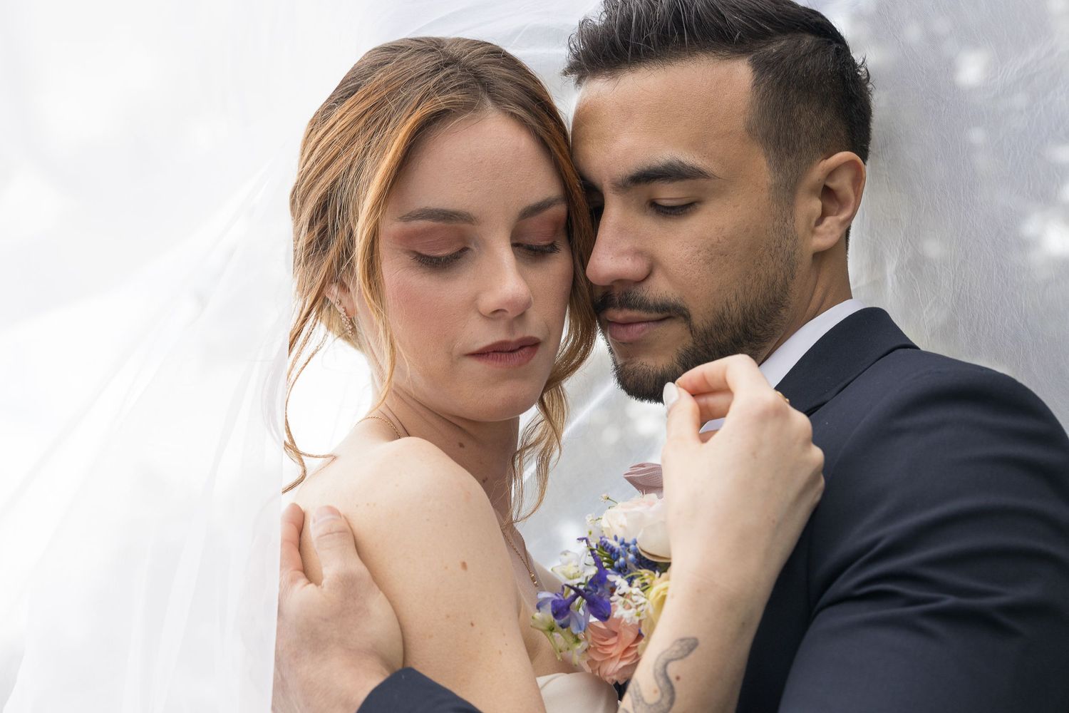 Tender wedding moment captured with couple in close embrace under sheer veil.