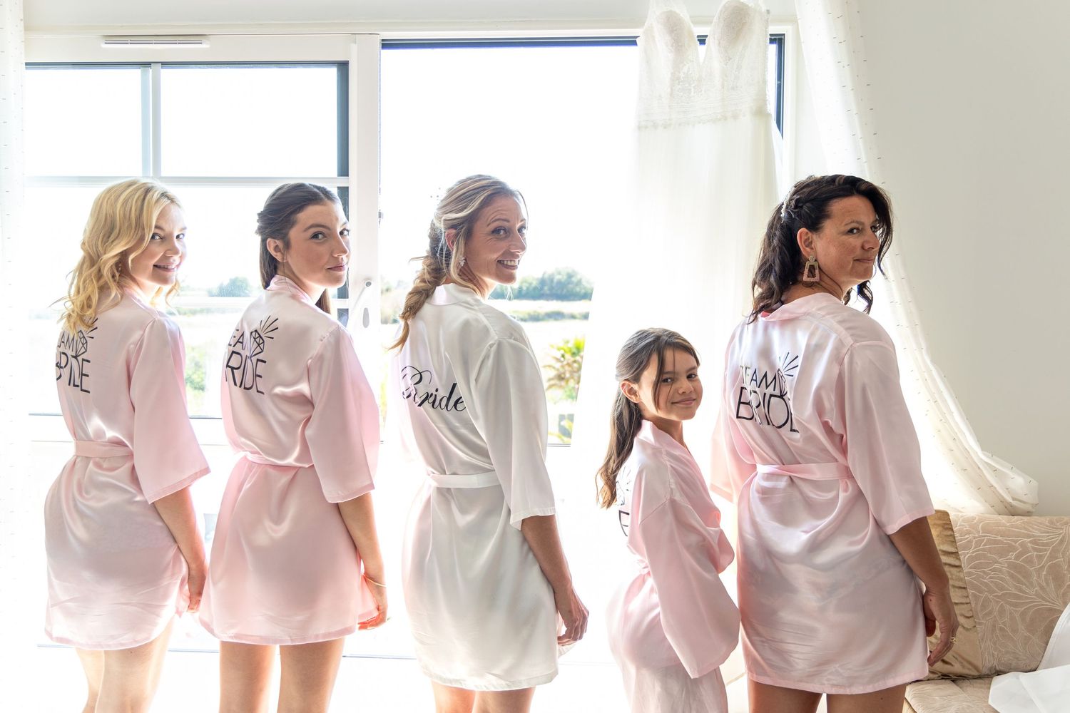 Wedding party laughs together while wearing matching white robes during preparation.