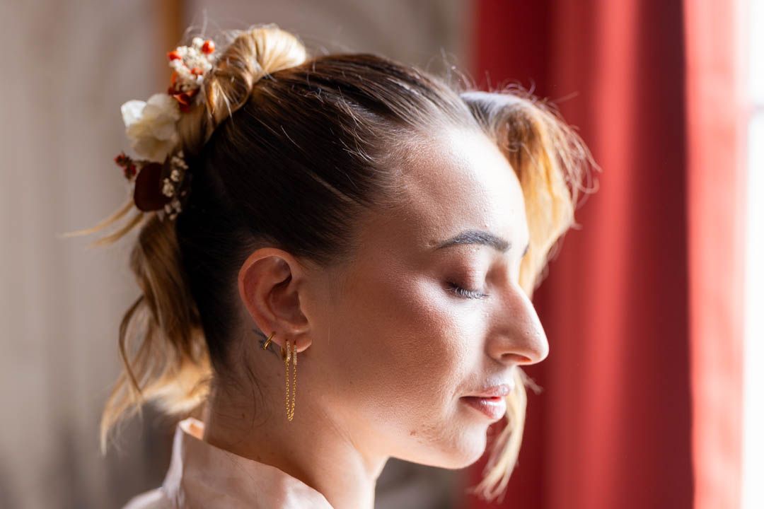 Woman with blonde hair pulled back looks into the distance against red curtain backdrop.