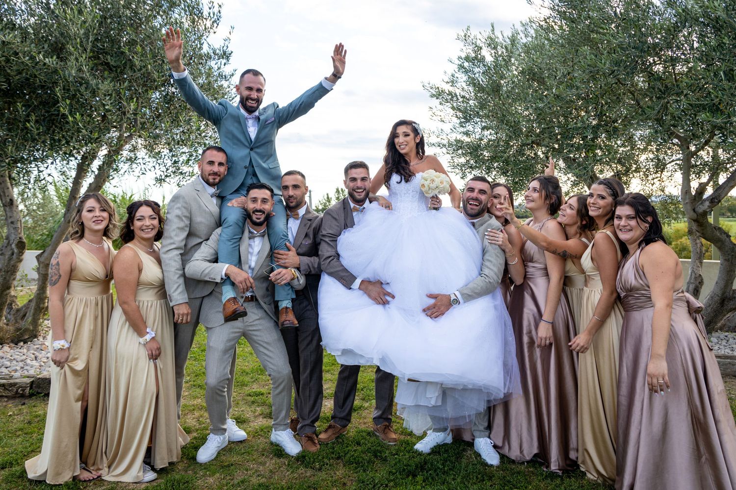 Wedding party celebrating outdoors among olive trees with bridal party in earth-toned dresses.