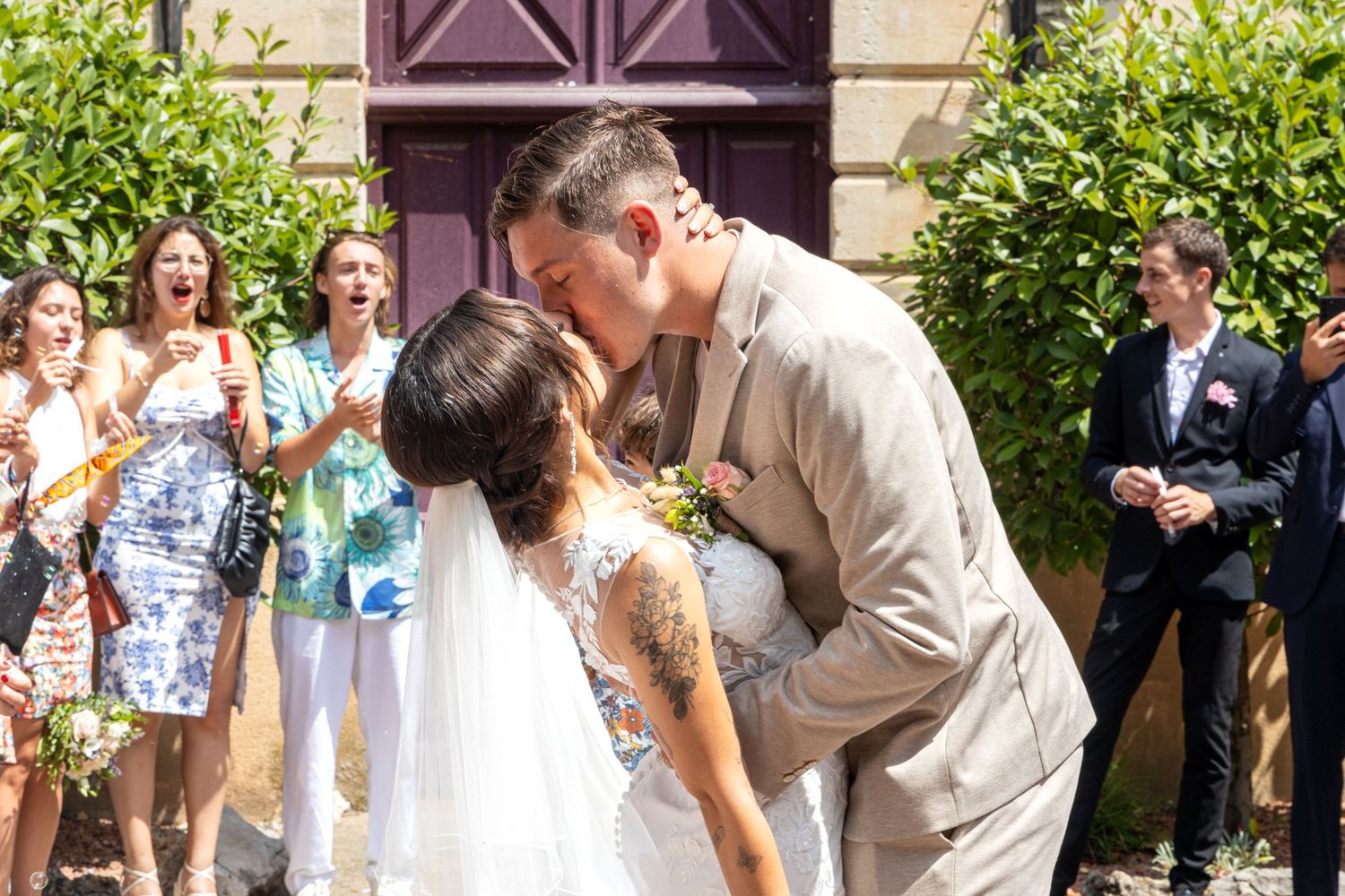 Couple shares romantic outdoor kiss during summer wedding ceremony.