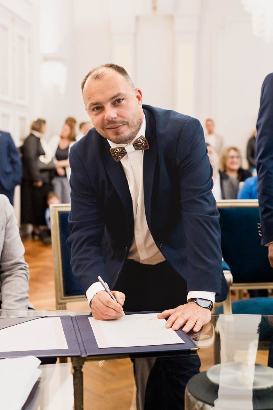 Man in formal suit signing official documents at ceremony venue.