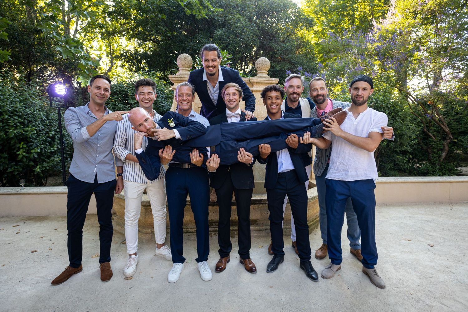 A group of groomsmen lift the groom during an outdoor wedding photo session.