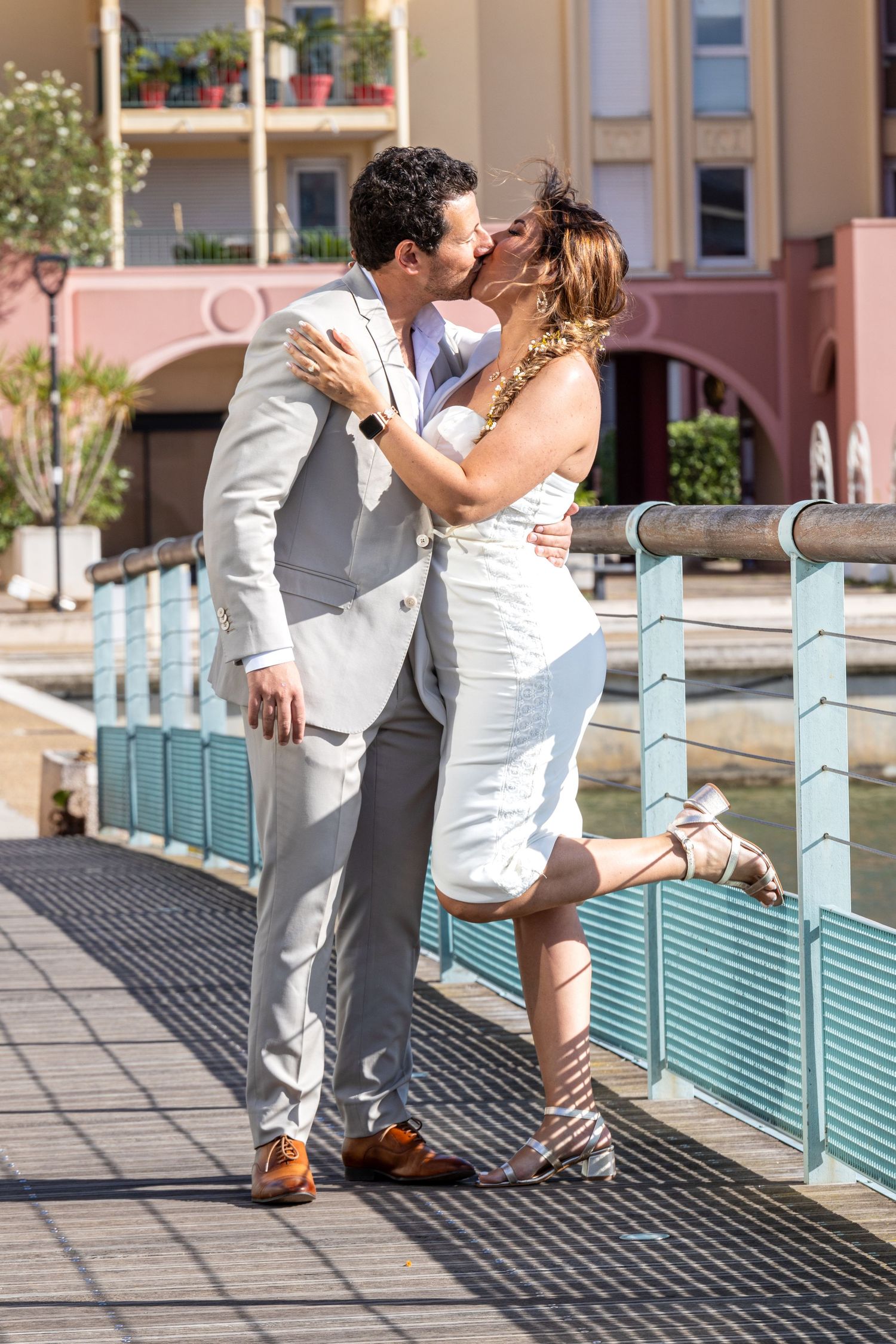 Romantic couple in white attire embracing on a Mediterranean-style resort bridge.