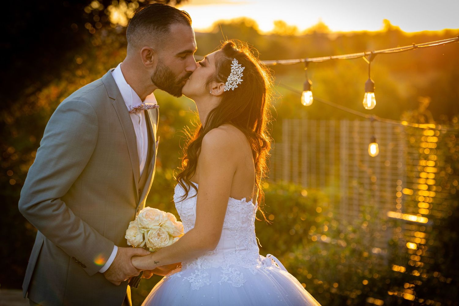 Romantic wedding photo shoot at sunset with soft golden lighting and white string lights in background.