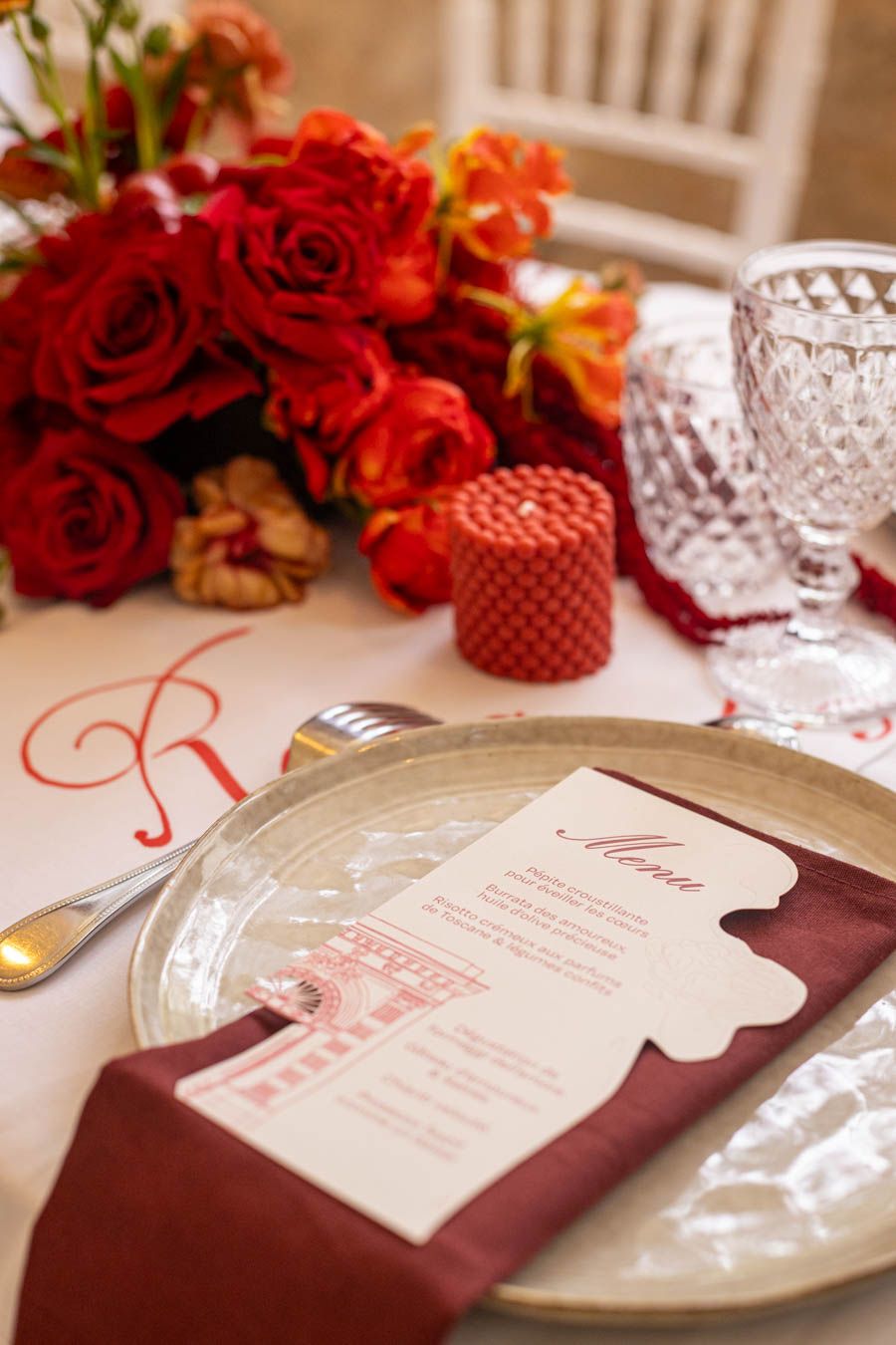 Elegant place setting with burgundy napkin, menu card, and red rose centerpiece.