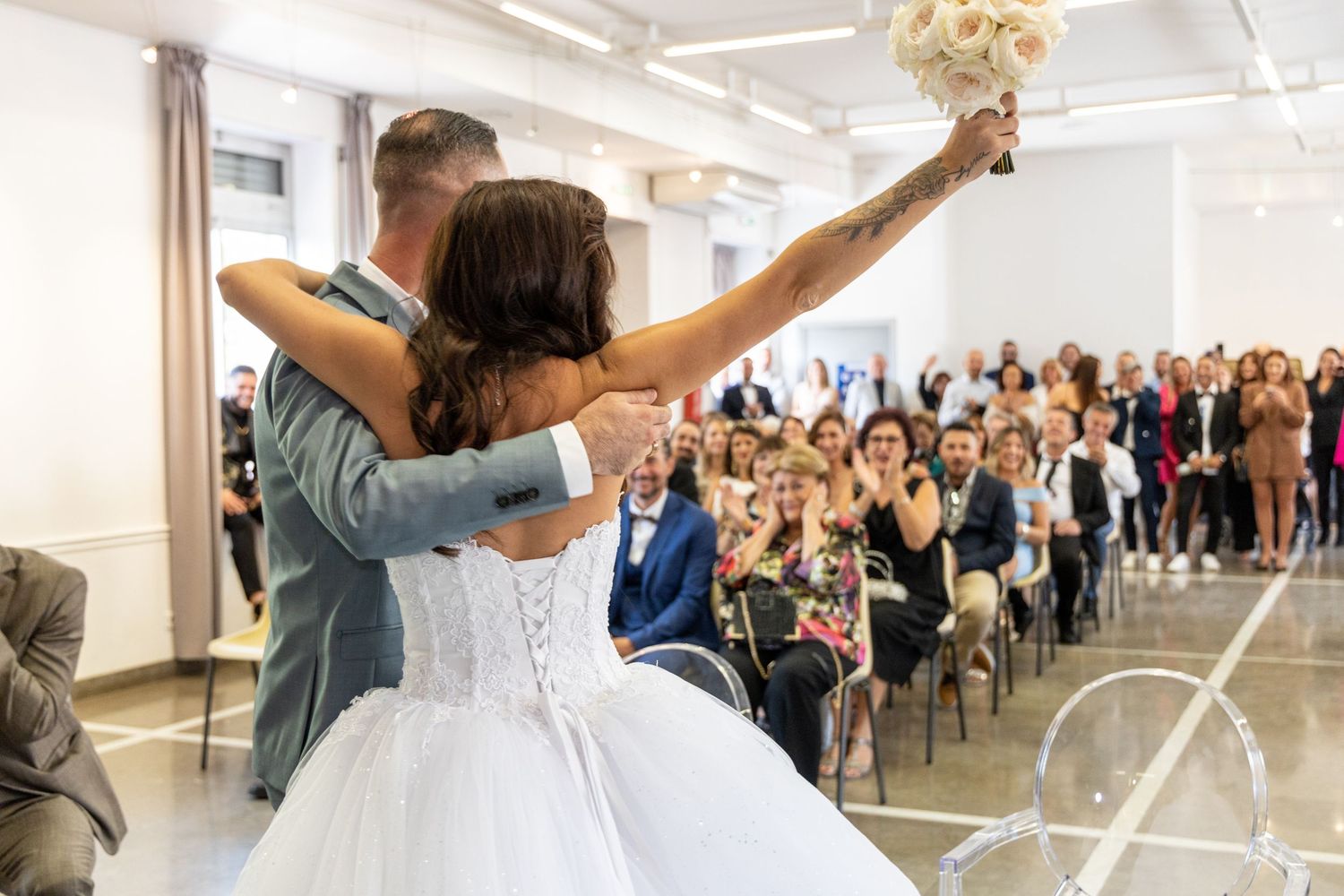 A wedding couple celebrates with arms raised while guests cheer in the background.