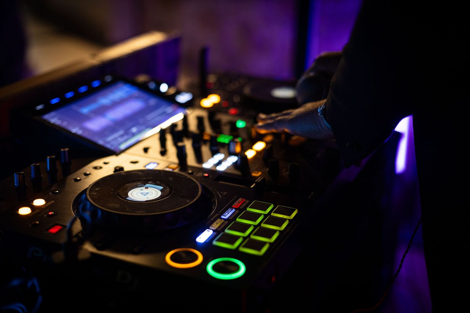 DJ equipment and controllers illuminated by purple lighting at a nighttime event.