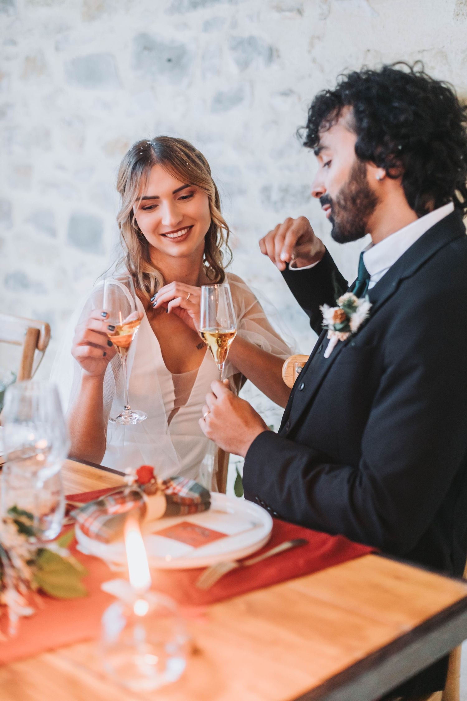 Romantic candlelit moment between couple clinking champagne glasses at wedding dinner.