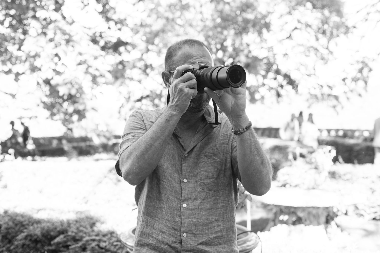 Black and white portrait of photographer taking photo with professional camera outdoors.