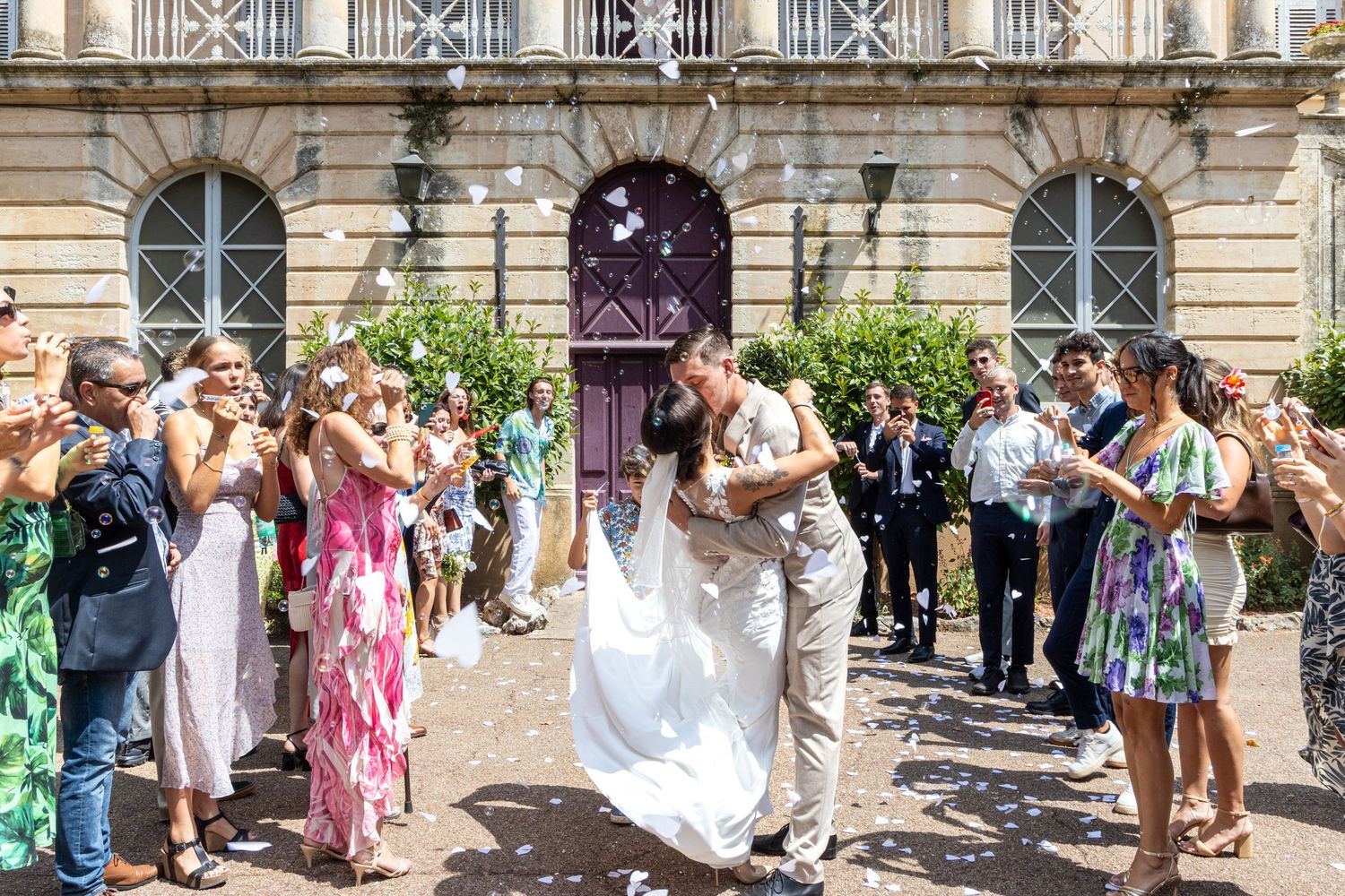 Wedding party and guests celebrating outside historic building with classical architecture.