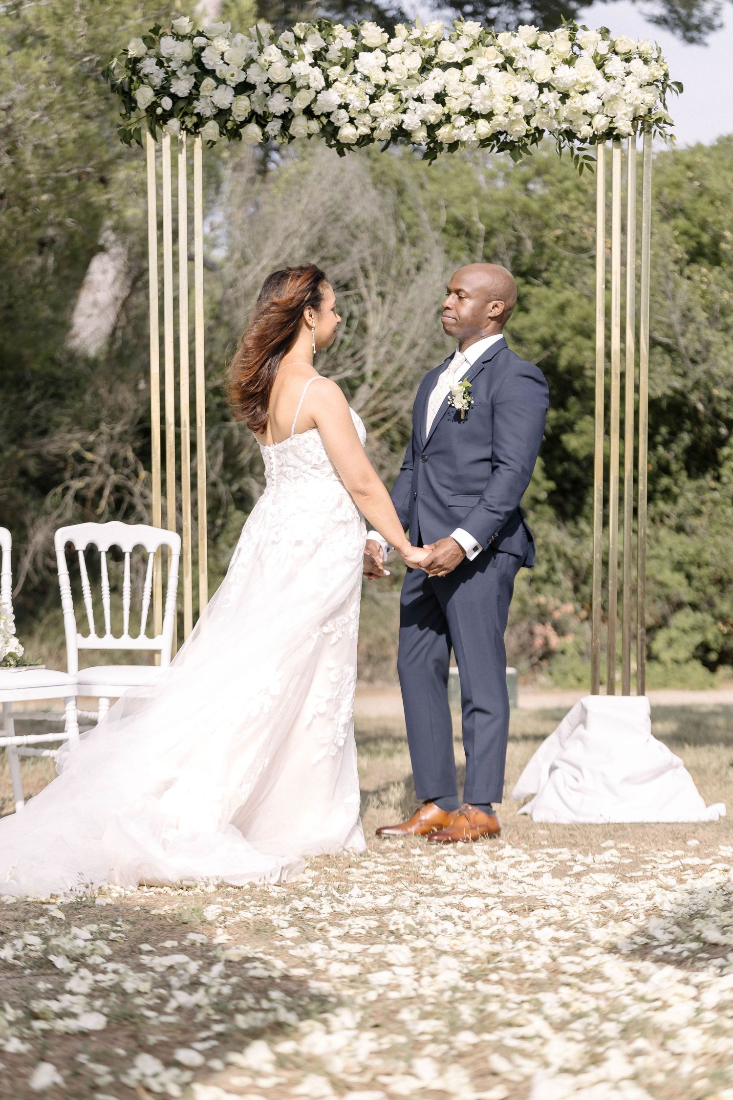 Wedding couple sitting and interacting in a garden setting with white floral decorations.