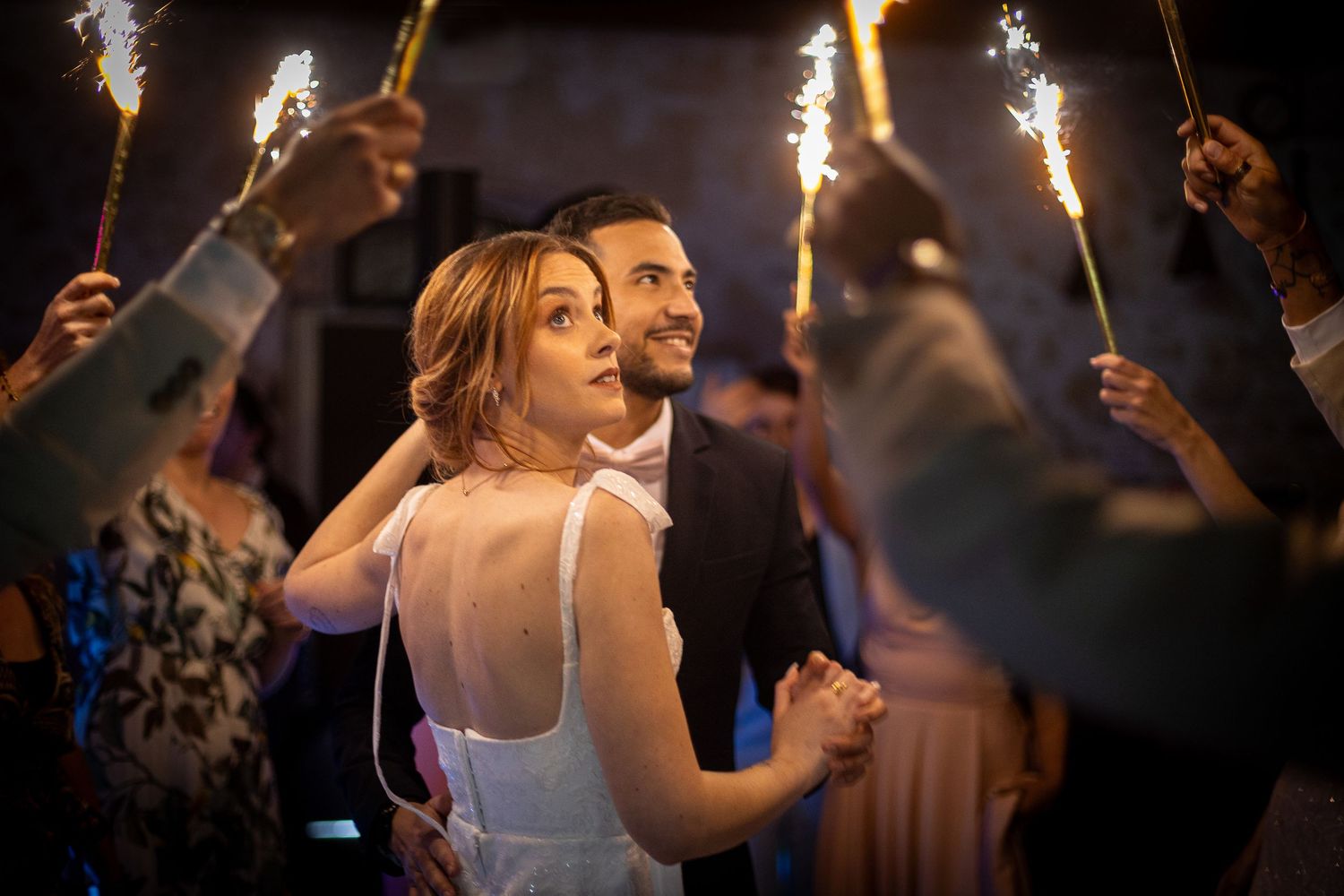 Wedding guests dance and celebrate on a dimly lit dance floor with raised sparklers creating a magical atmosphere.