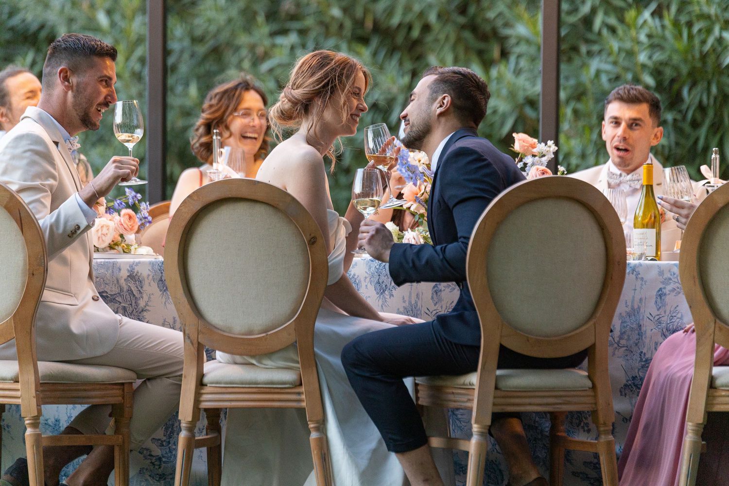 Outdoor wedding reception dinner with guests seated at elegant tables under garden greenery.