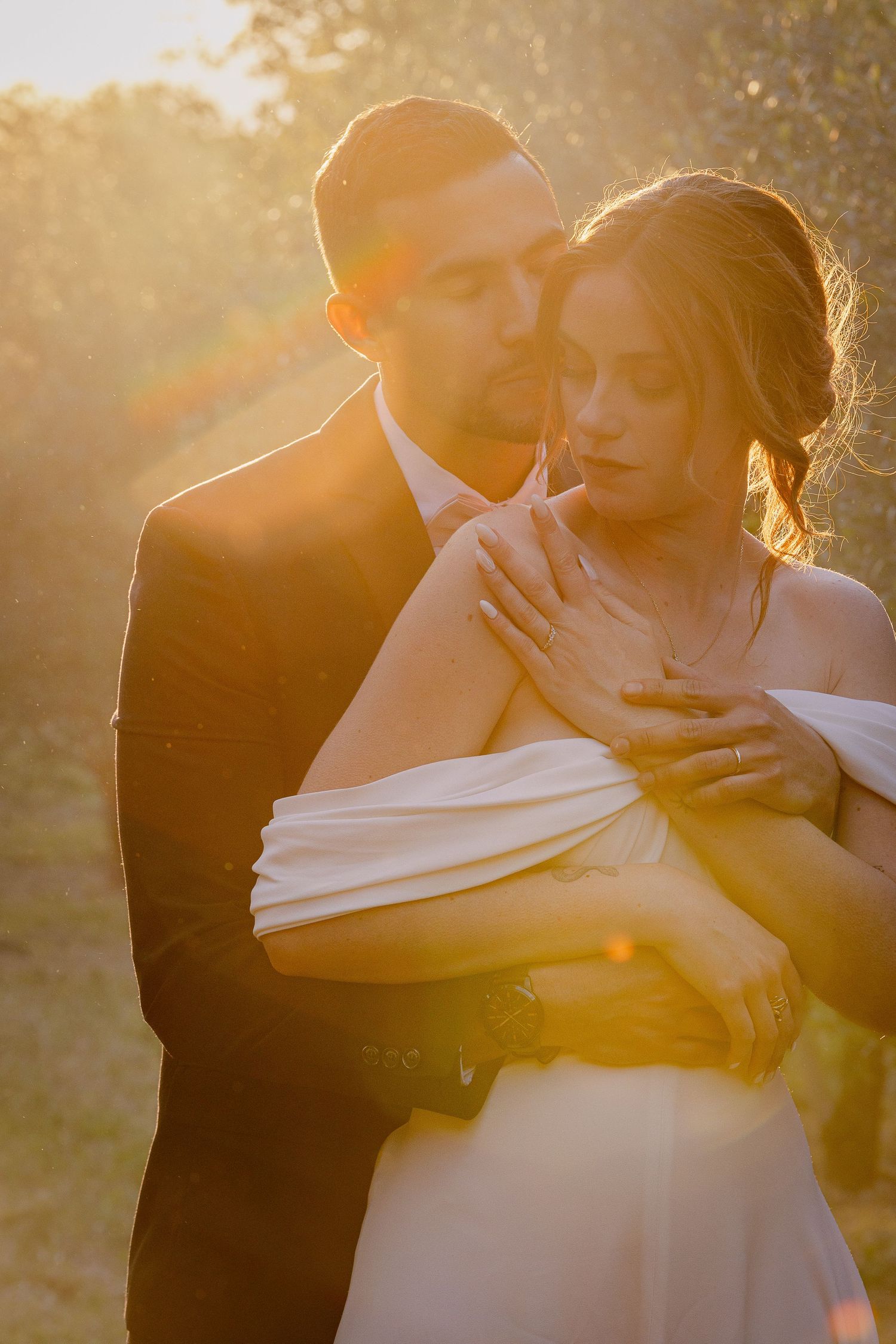 Romantic sunset wedding photo with couple embracing in golden light.