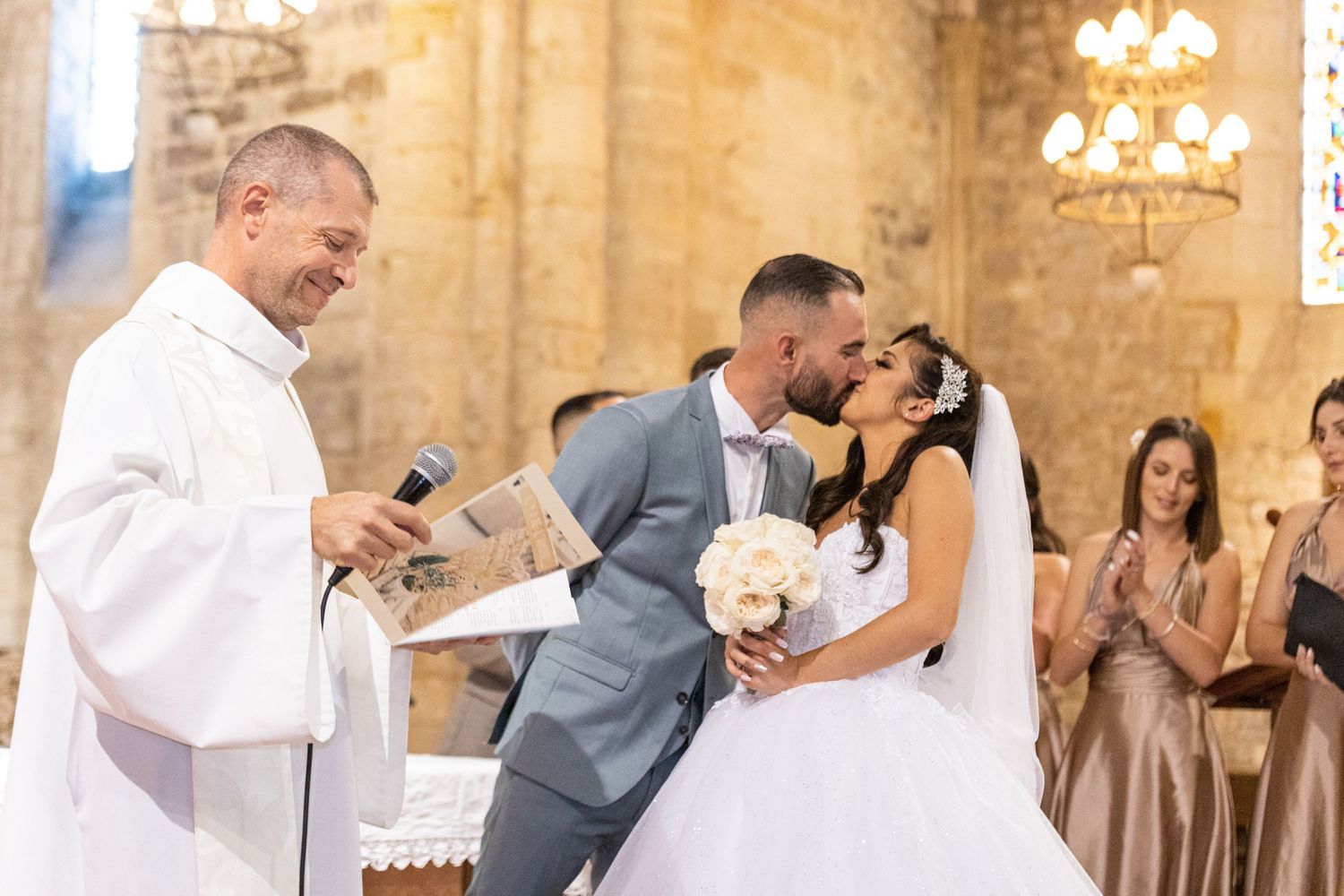 Wedding ceremony in progress inside an ancient stone church with elegant chandeliers.