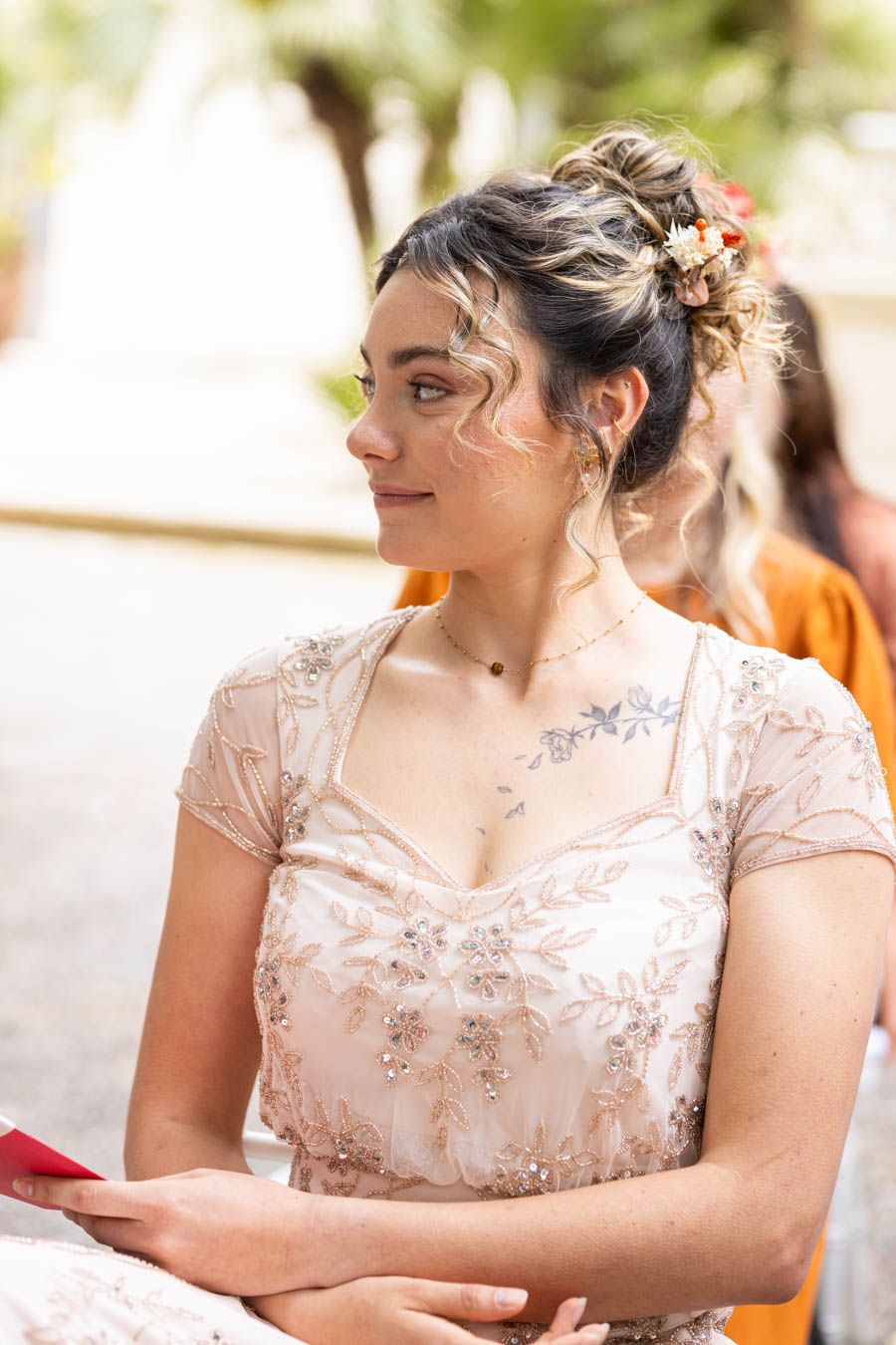 Woman in delicate lace dress sitting with thoughtful expression during a formal event.