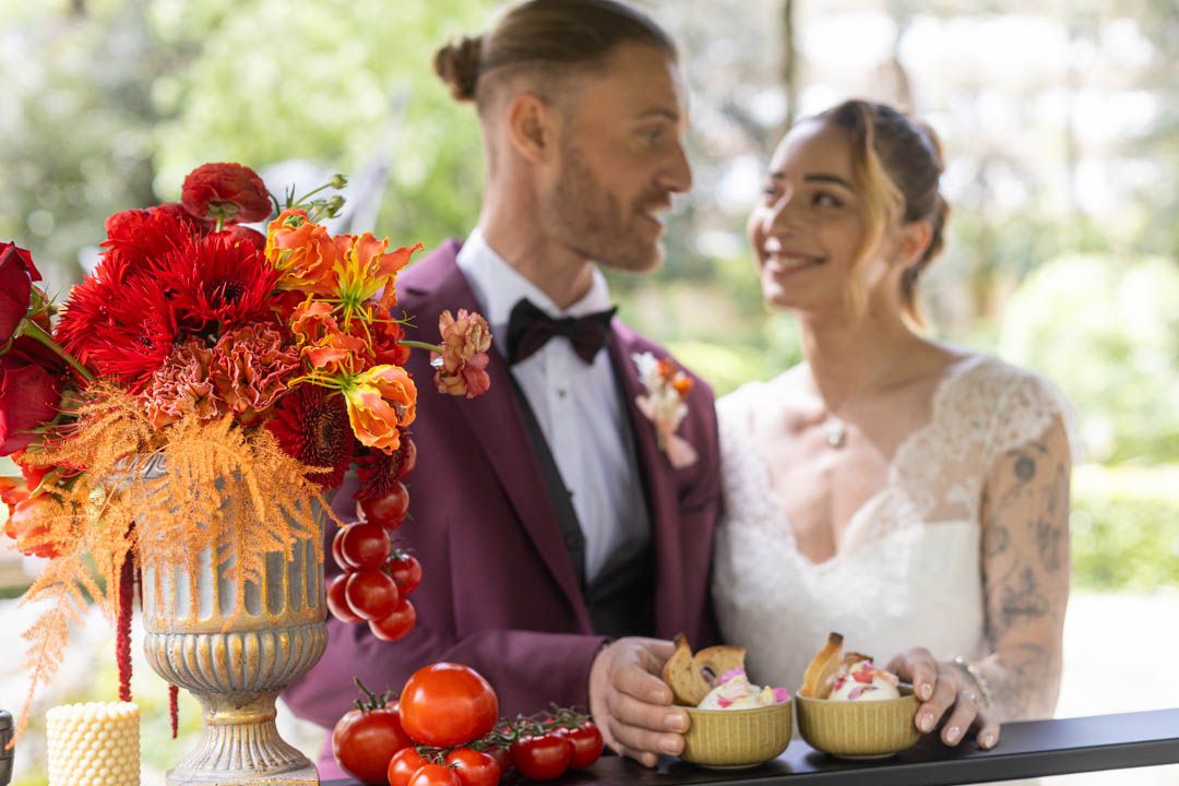 Outdoor wedding reception featuring burgundy decor and vibrant orange floral centerpieces.