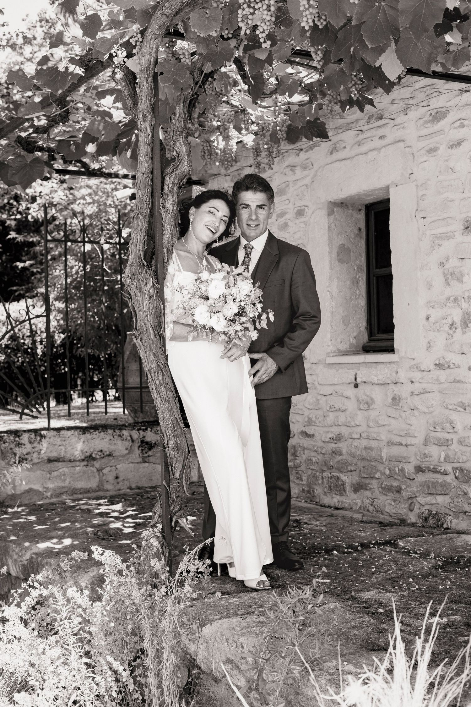 Artistic black and white wedding portraits taken against a rustic stone wall with foliage.