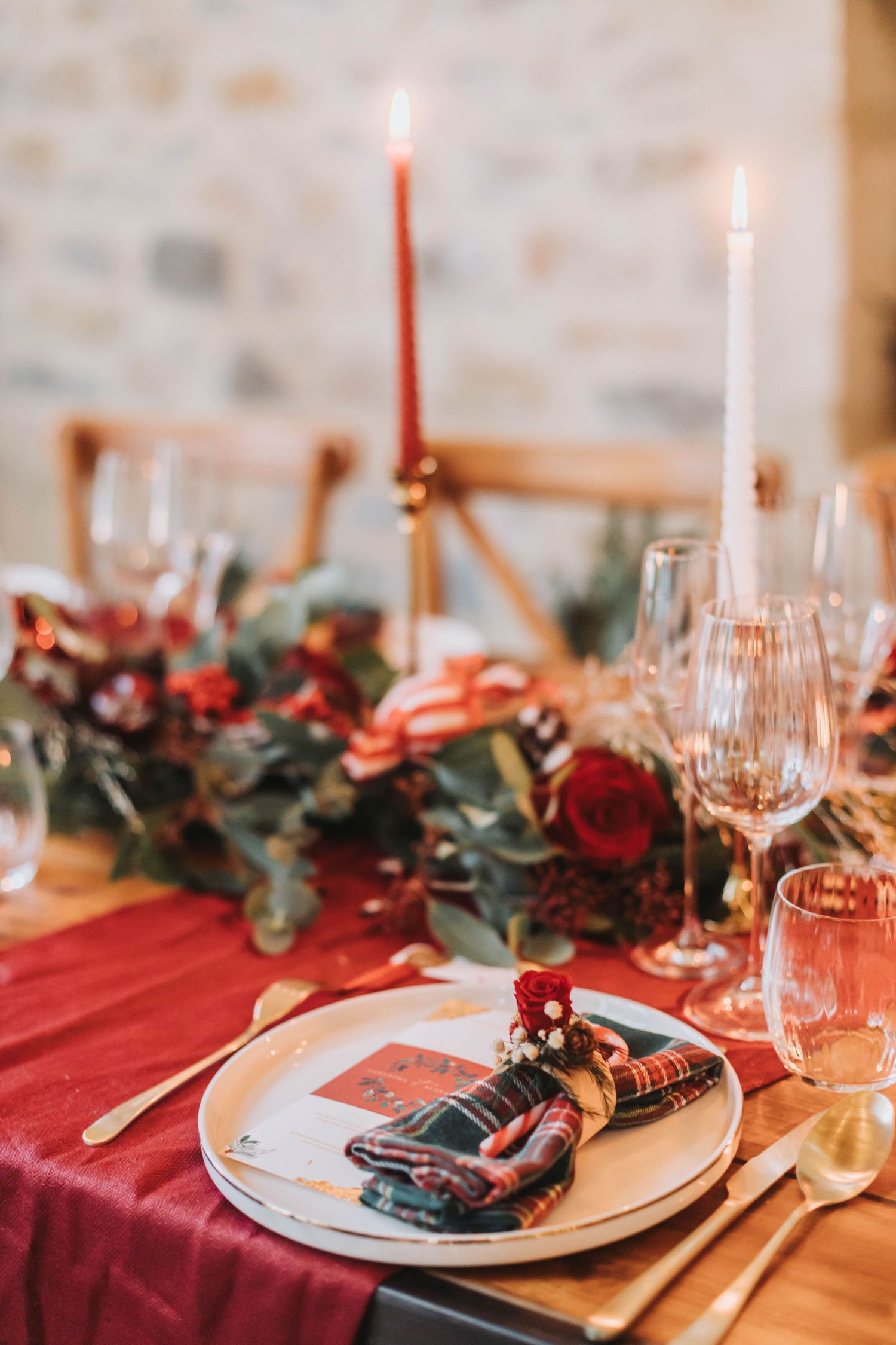 Elegant table setting with red tablecloth, candles, roses and eucalyptus centerpiece.