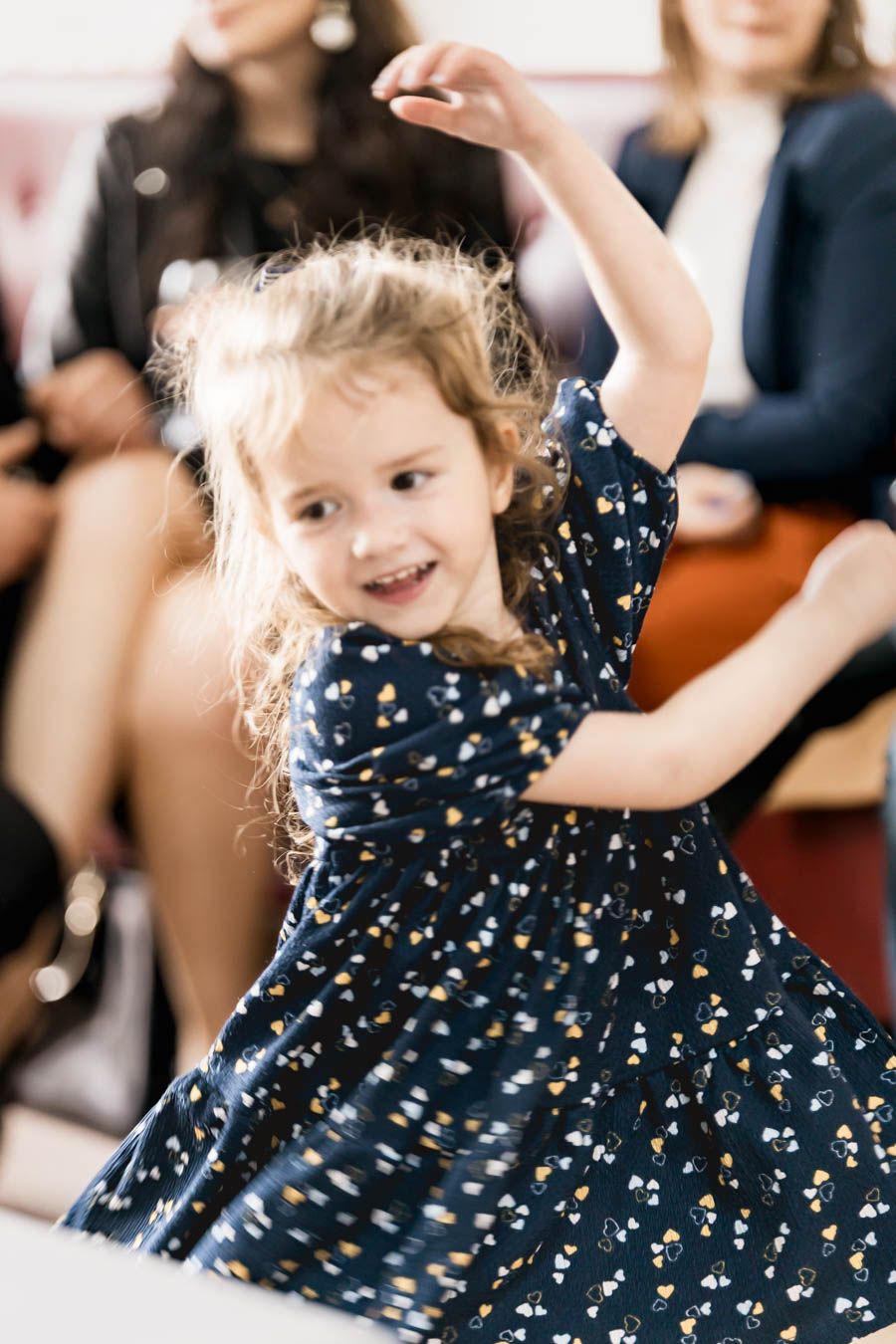 Young child in navy polka dot dress twirling and dancing at wedding reception.