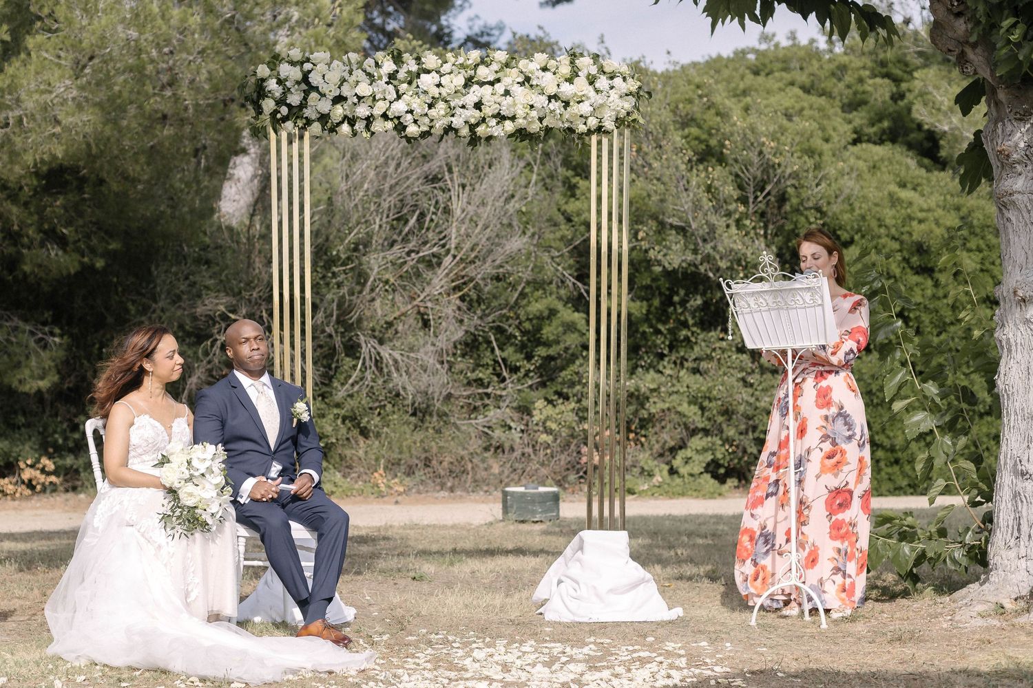Wedding ceremony setup in a garden with gold arch and white flowers.