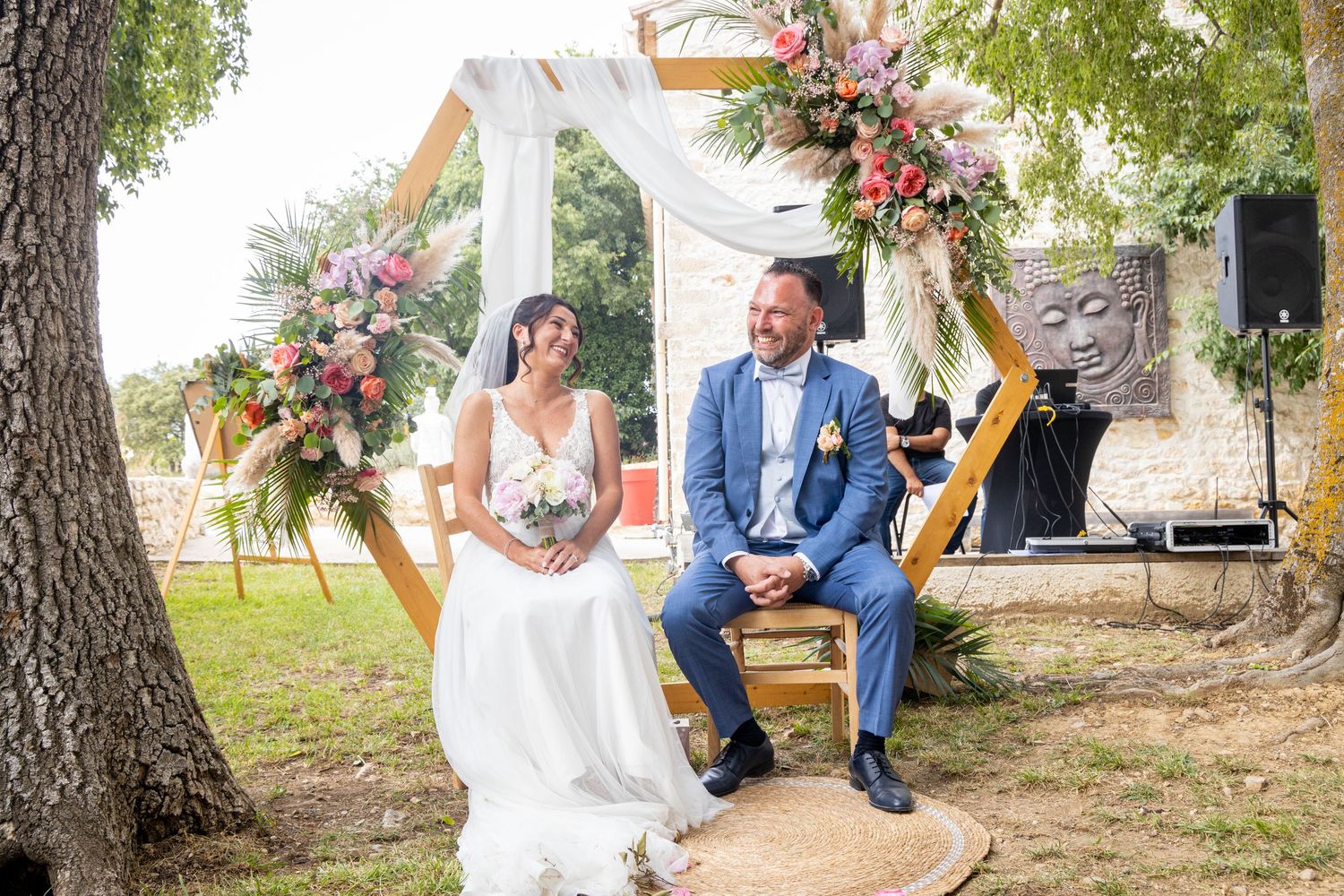 Outdoor wedding ceremony setup with rows of white chairs under trees and floral decorations.