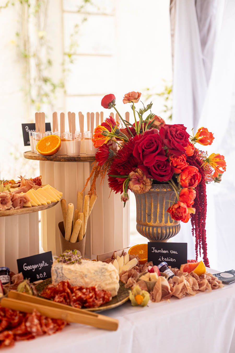 Elegant wedding reception table with red floral arrangements and charcuterie display.