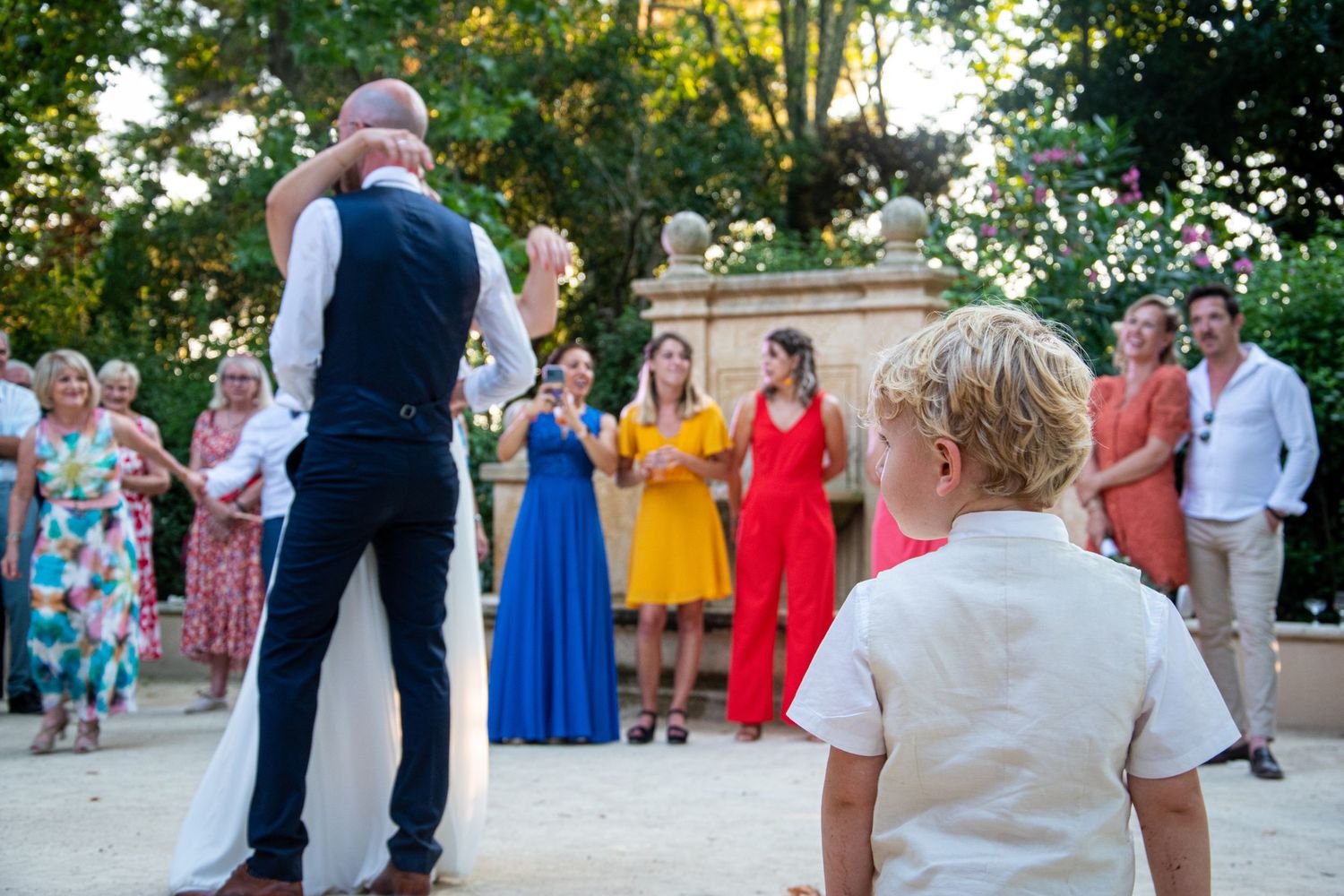 Wedding guests in vibrant dresses watch a couple dancing at an outdoor reception.