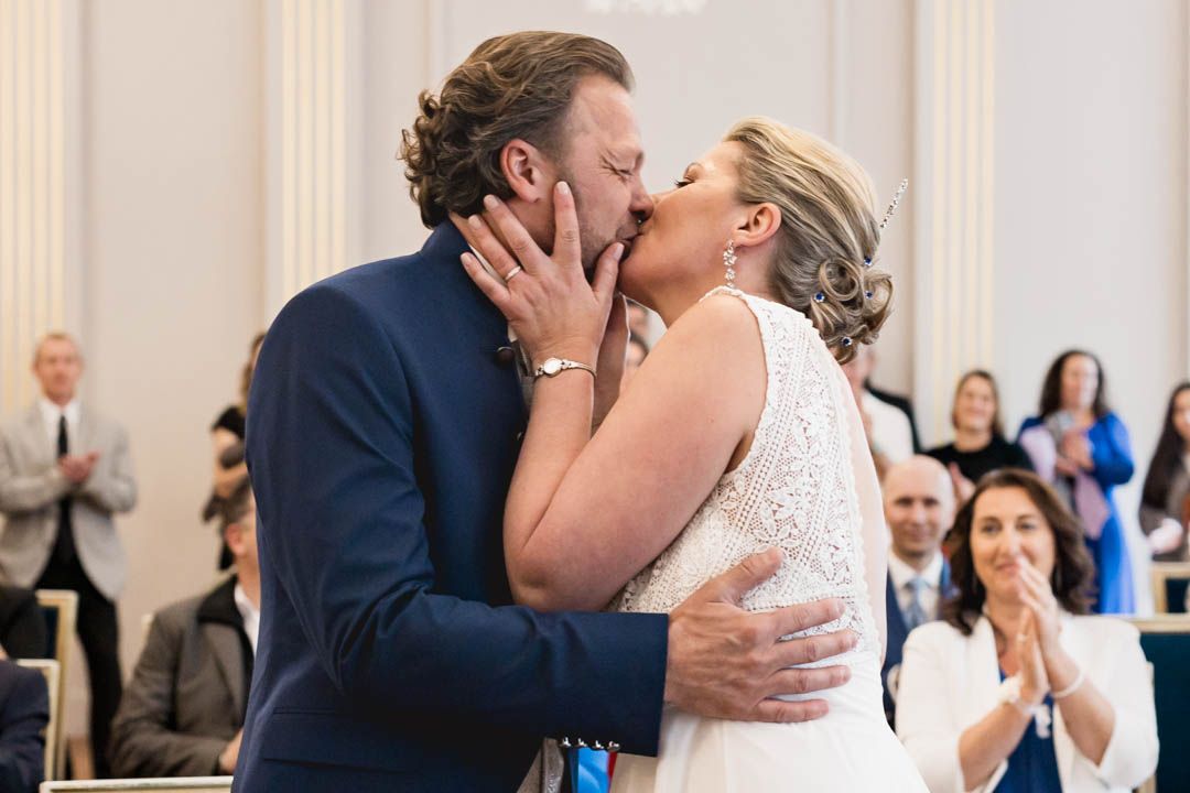 A tender wedding ceremony kiss moment captured in an elegant white-columned venue.
