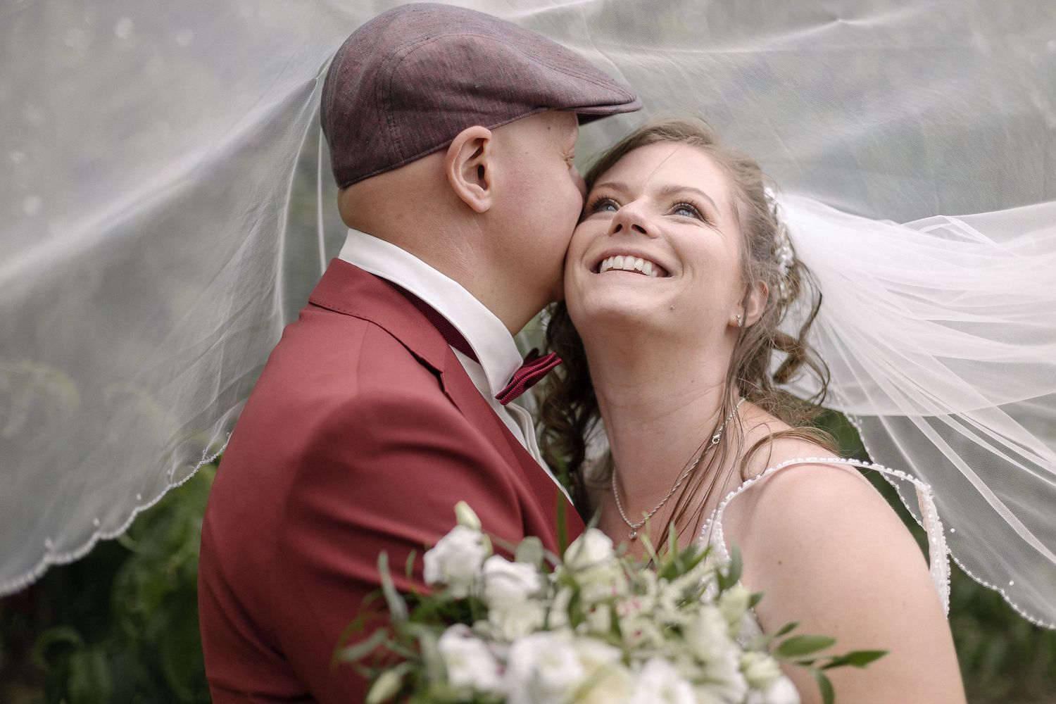 Joyful wedding couple shares a tender moment under flowing veil.