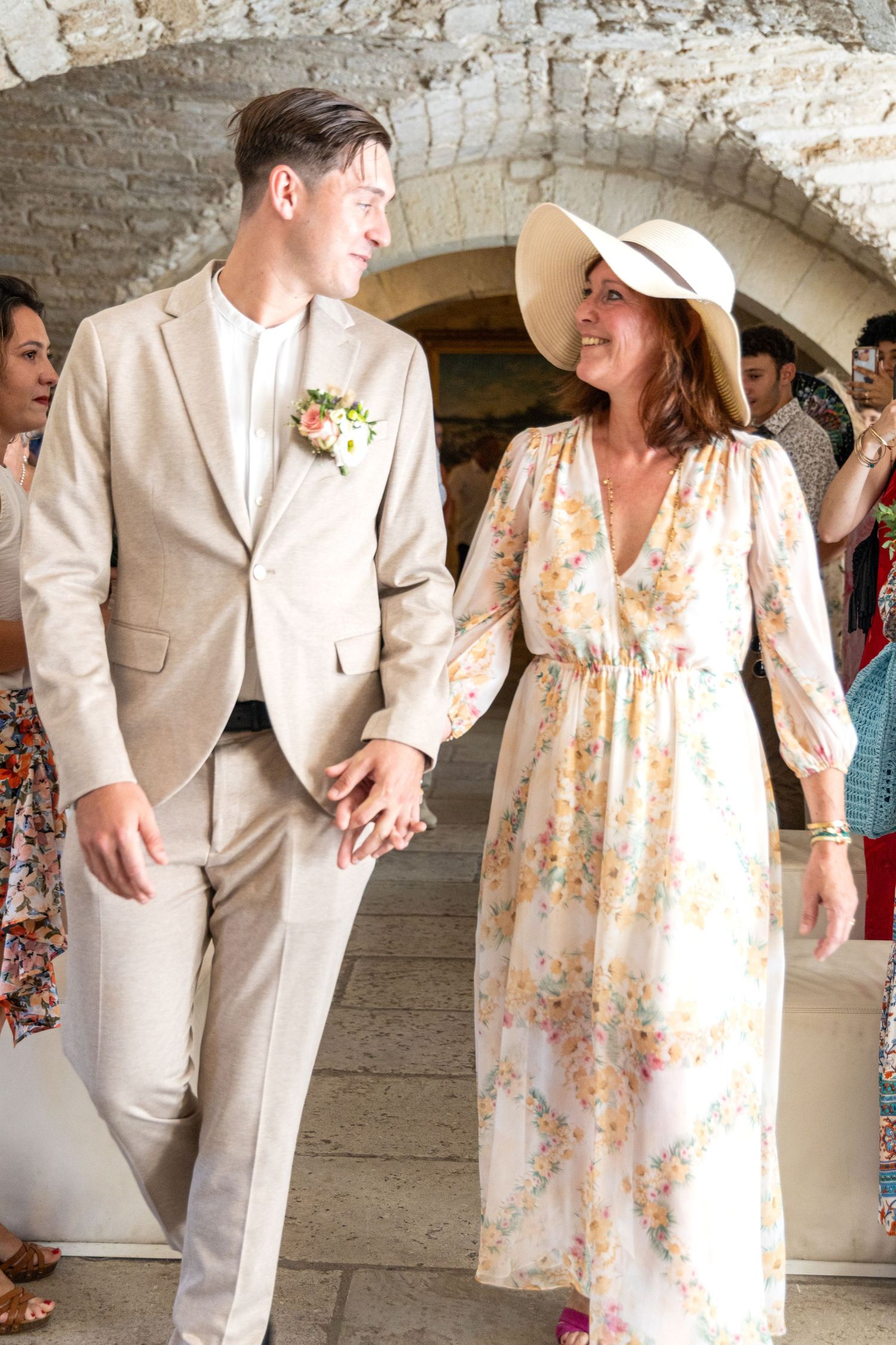 Wedding guests in summer attire walk through a historic stone corridor.
