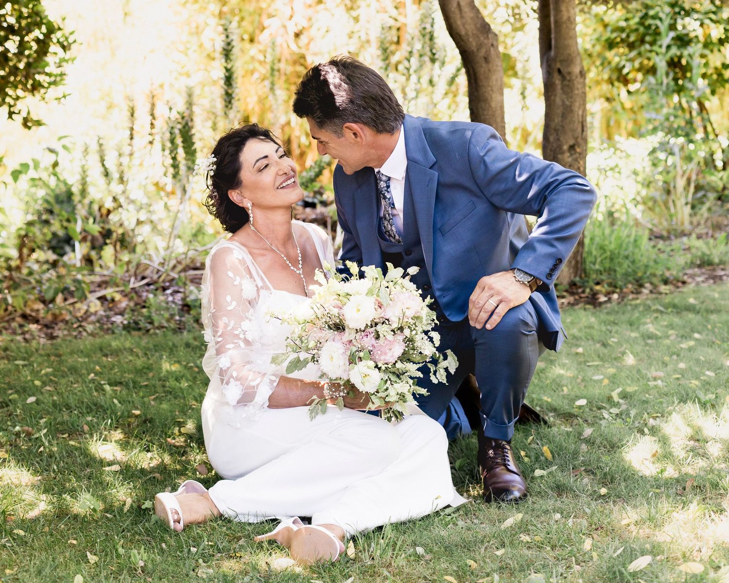 Romantic wedding couple lying on grass surrounded by greenery during outdoor photo session.