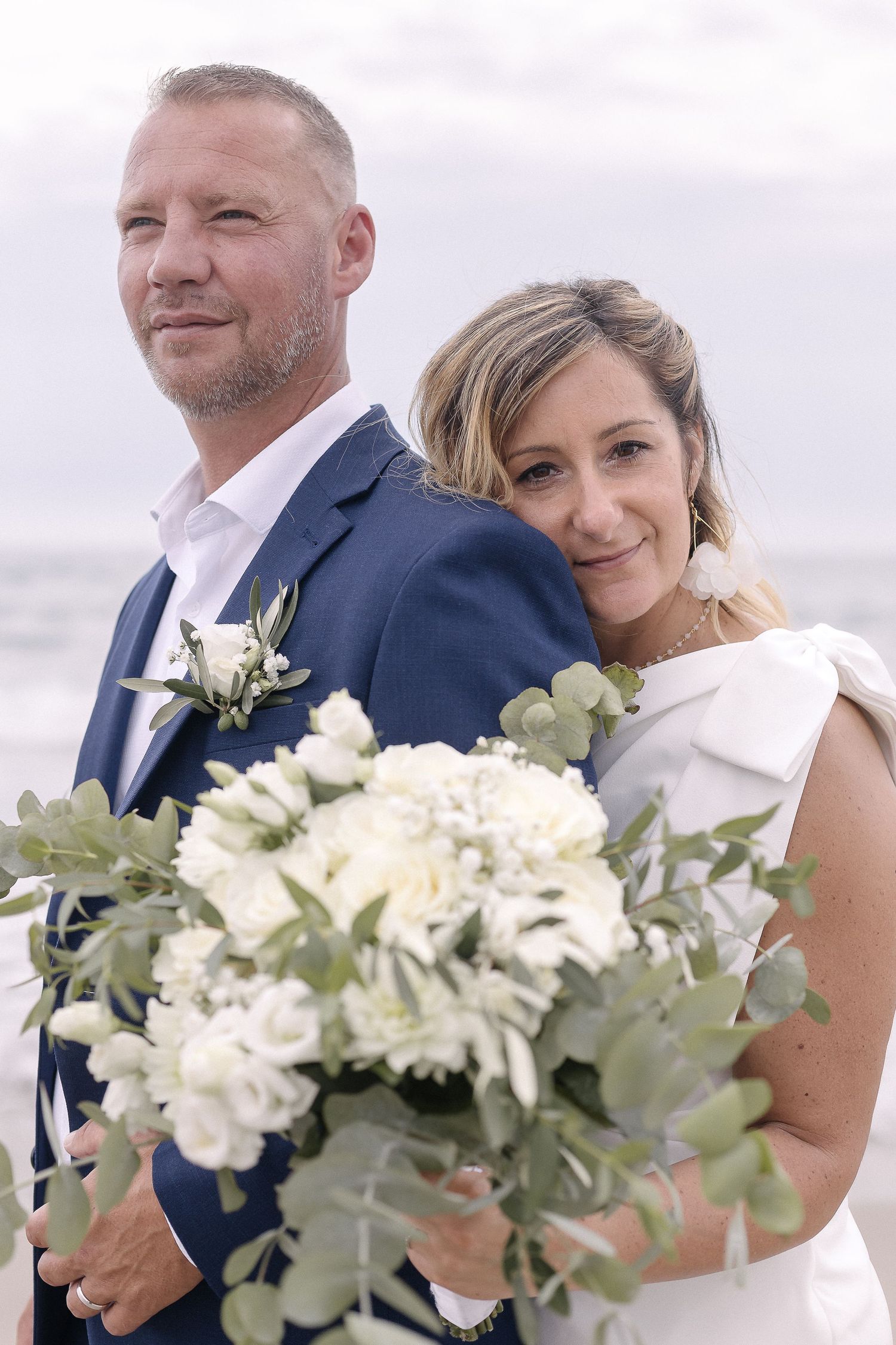 Seaside wedding portrait with white floral bouquet and natural coastal lighting.