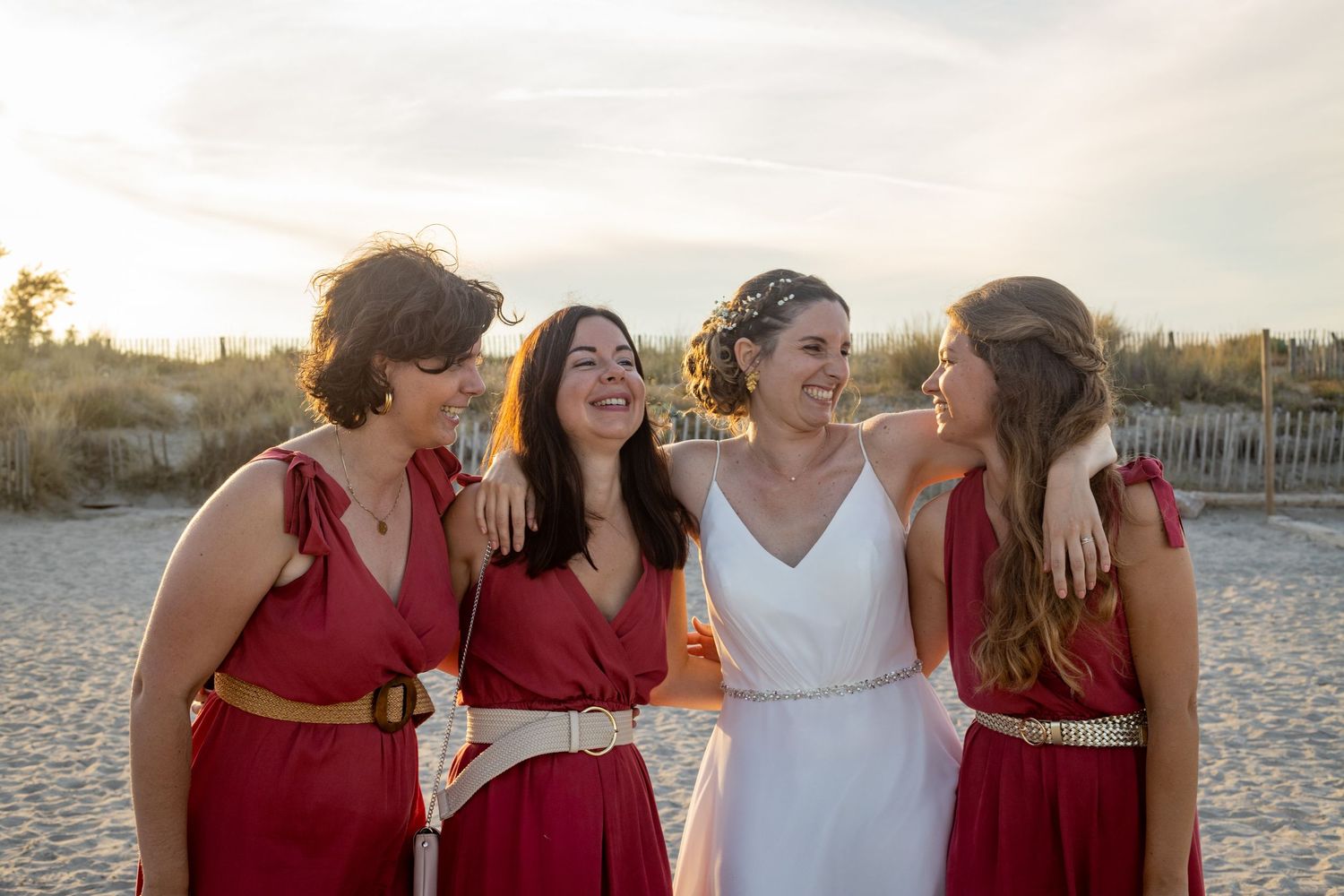 Wedding party in red and white dresses posing on a beach at sunset.