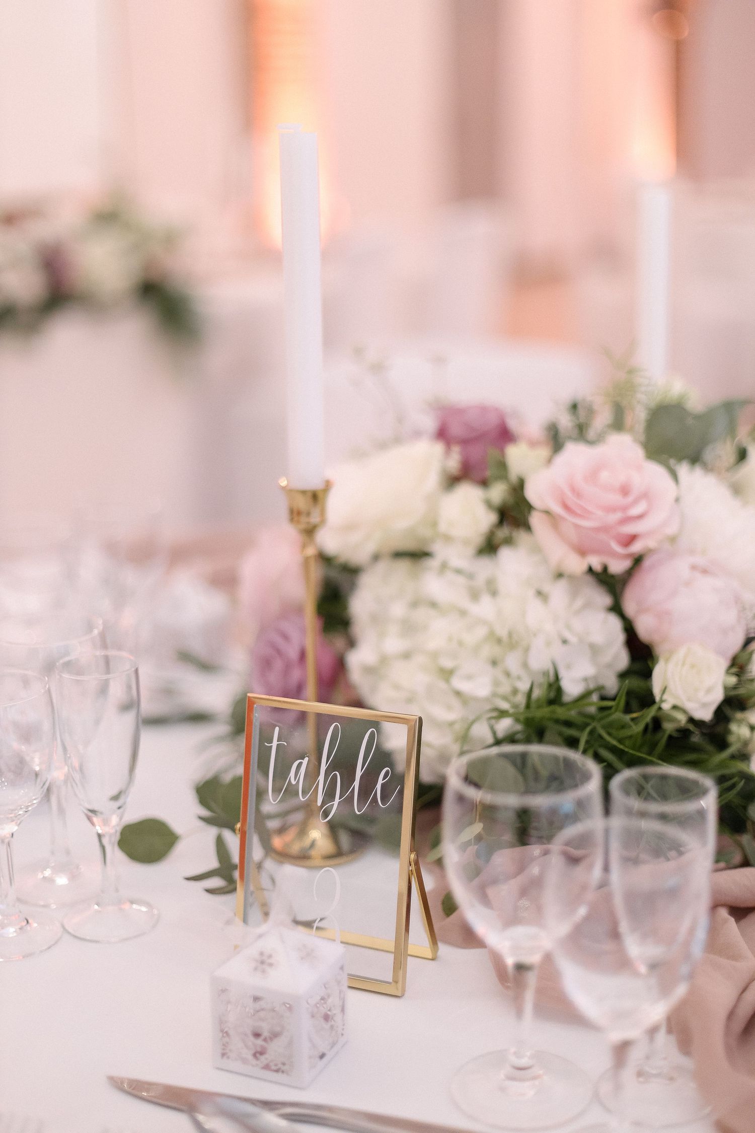 Elegant table setting with pink and white flowers, candles, and gold-framed table numbers.