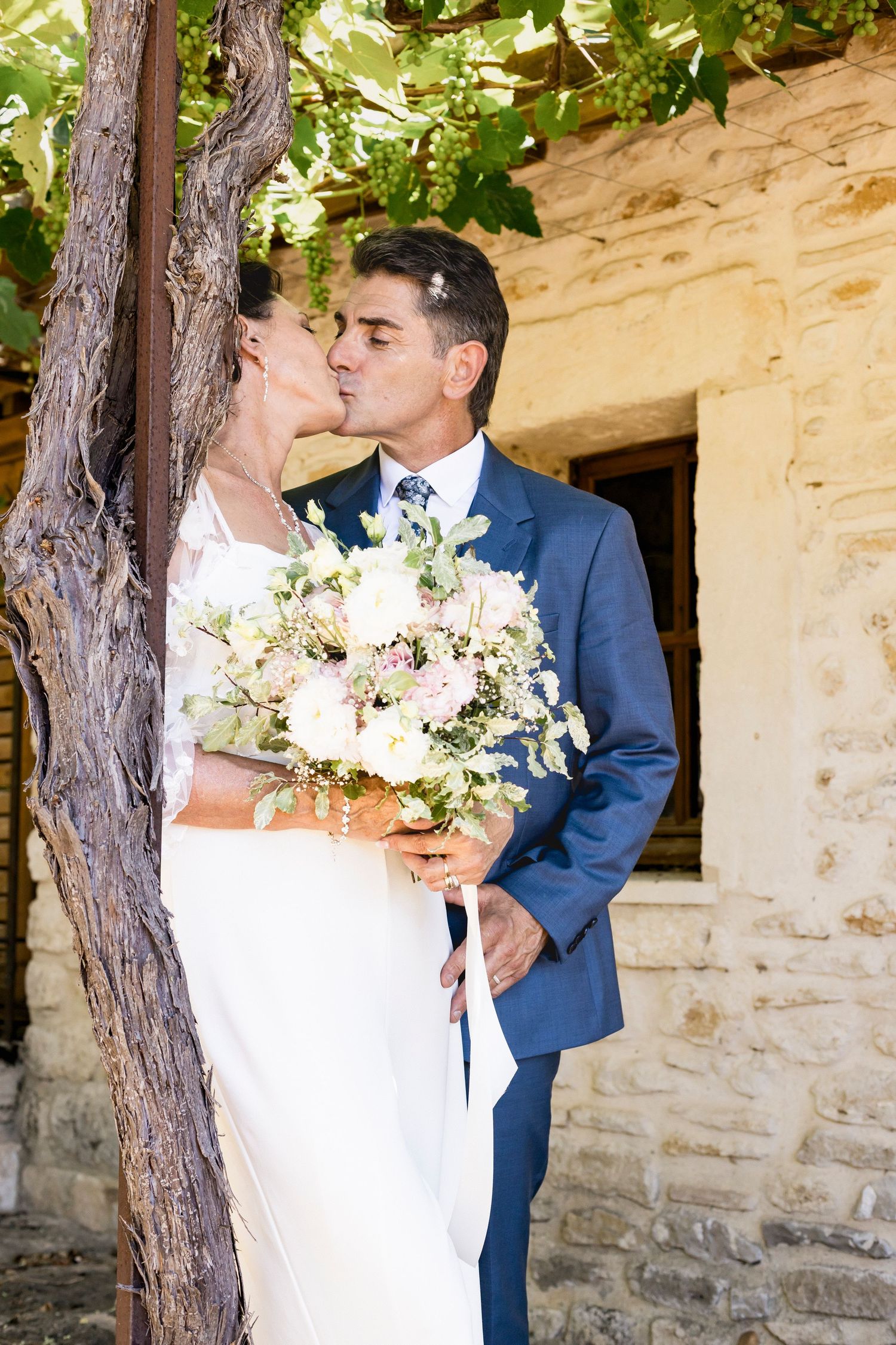 Newlyweds share tender moments while holding a bouquet of white and pink flowers.